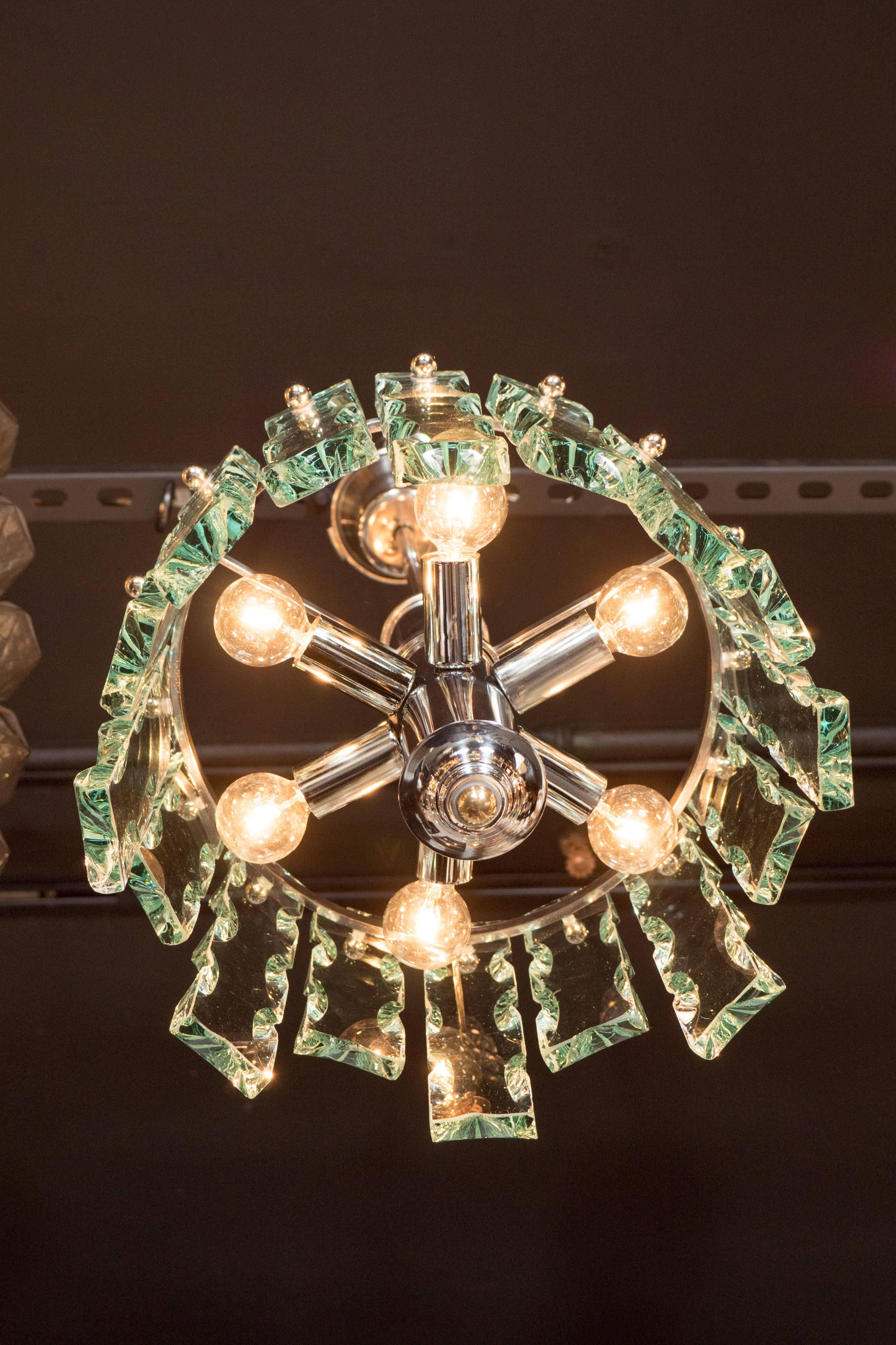 A Mid-Century Modernist chiseled glass chandelier in the style of Fontana Arte. Hand-cut, hand-chipped glass segments are suspended by polished chrome ball fittings in a staggered manner around a polished chrome frame. Light is emitted from six