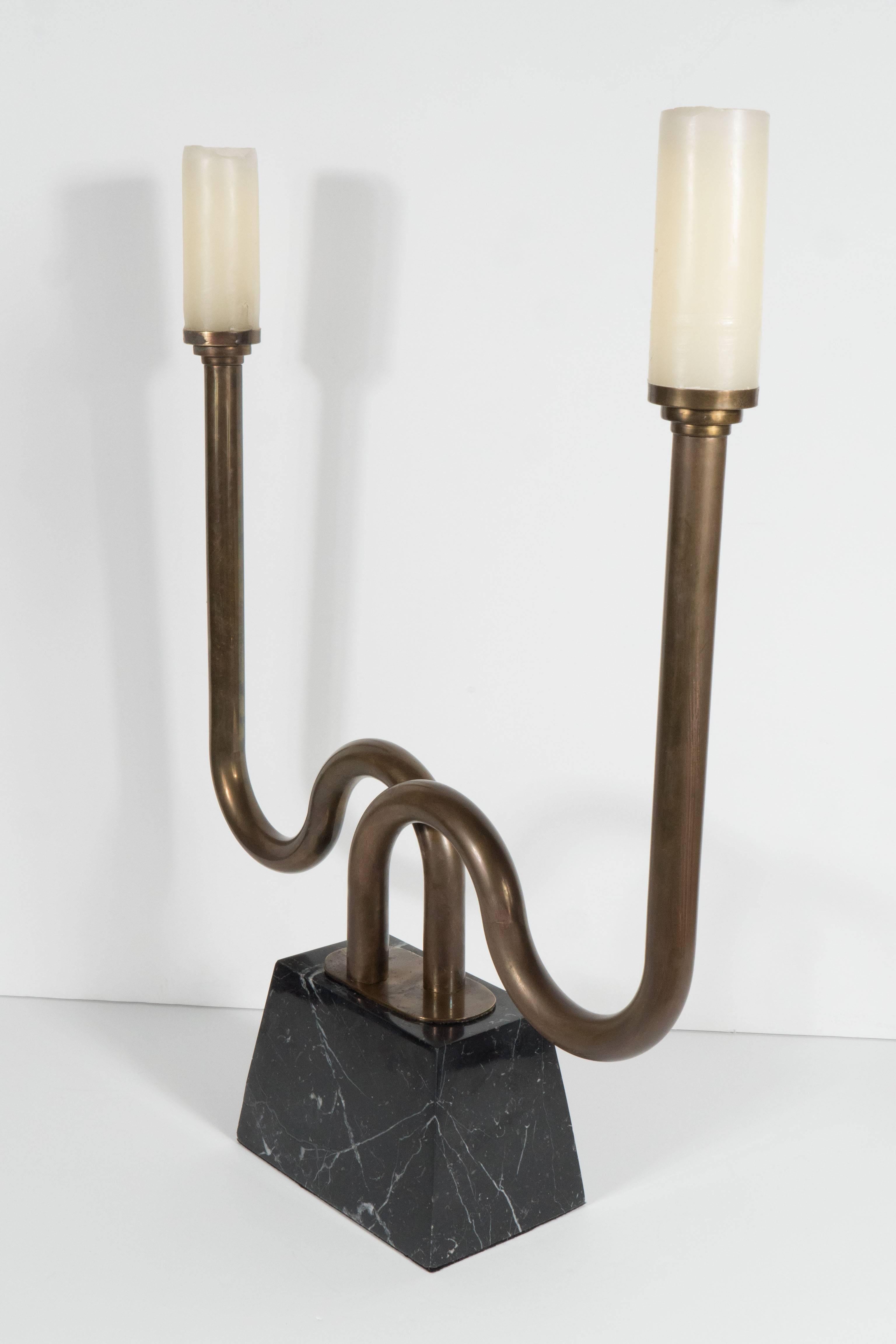 A sculptural pair of Mid-Century bronze candlesticks on polished black marble bases. Criss-crossing tubes of bronze each support cylindrical candles up to 2