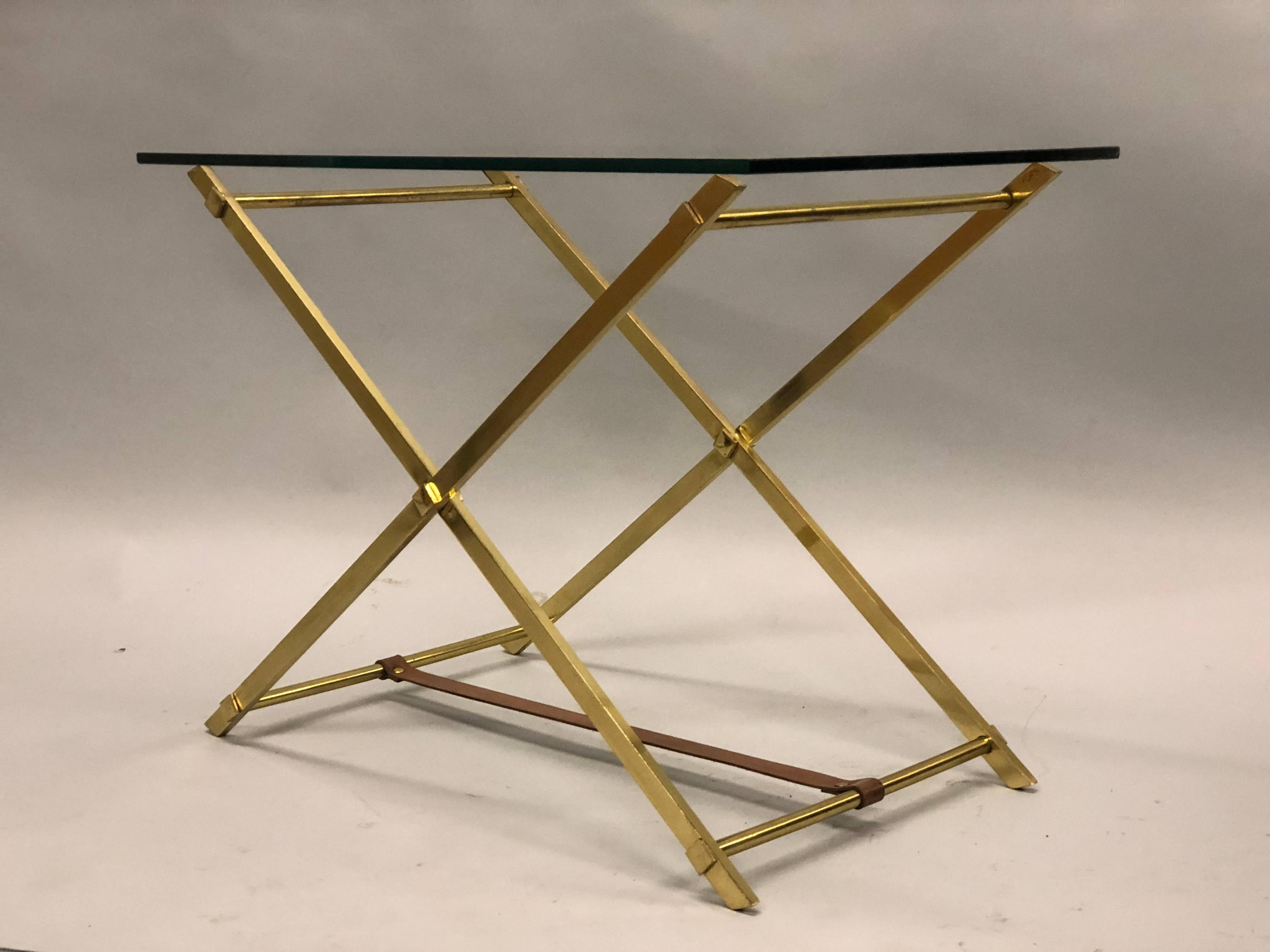 Elegant pair of French Mid-Century Modern neoclassical end tables by Hermes with solid brass frames in an X-frame form united by a leather stretcher supporting glass tops.