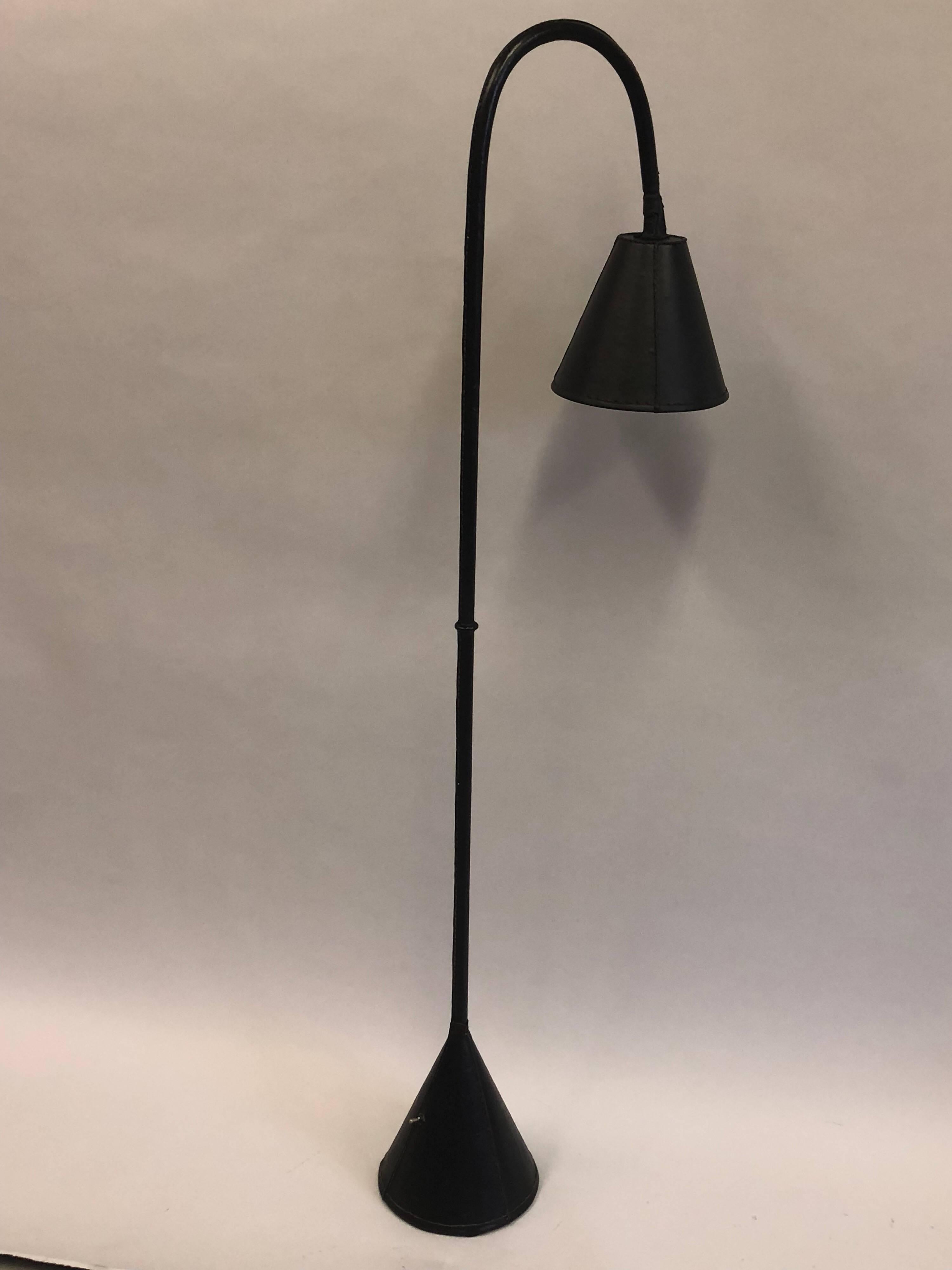 Elegant and timeless pair of French Mid-Century Modern hand stitched black leather floor lamps by Jacques Adnet. The standing lamps have a stunning form featuring a cone base with a dramatic curving stem terminating in a cone shade. Each piece is