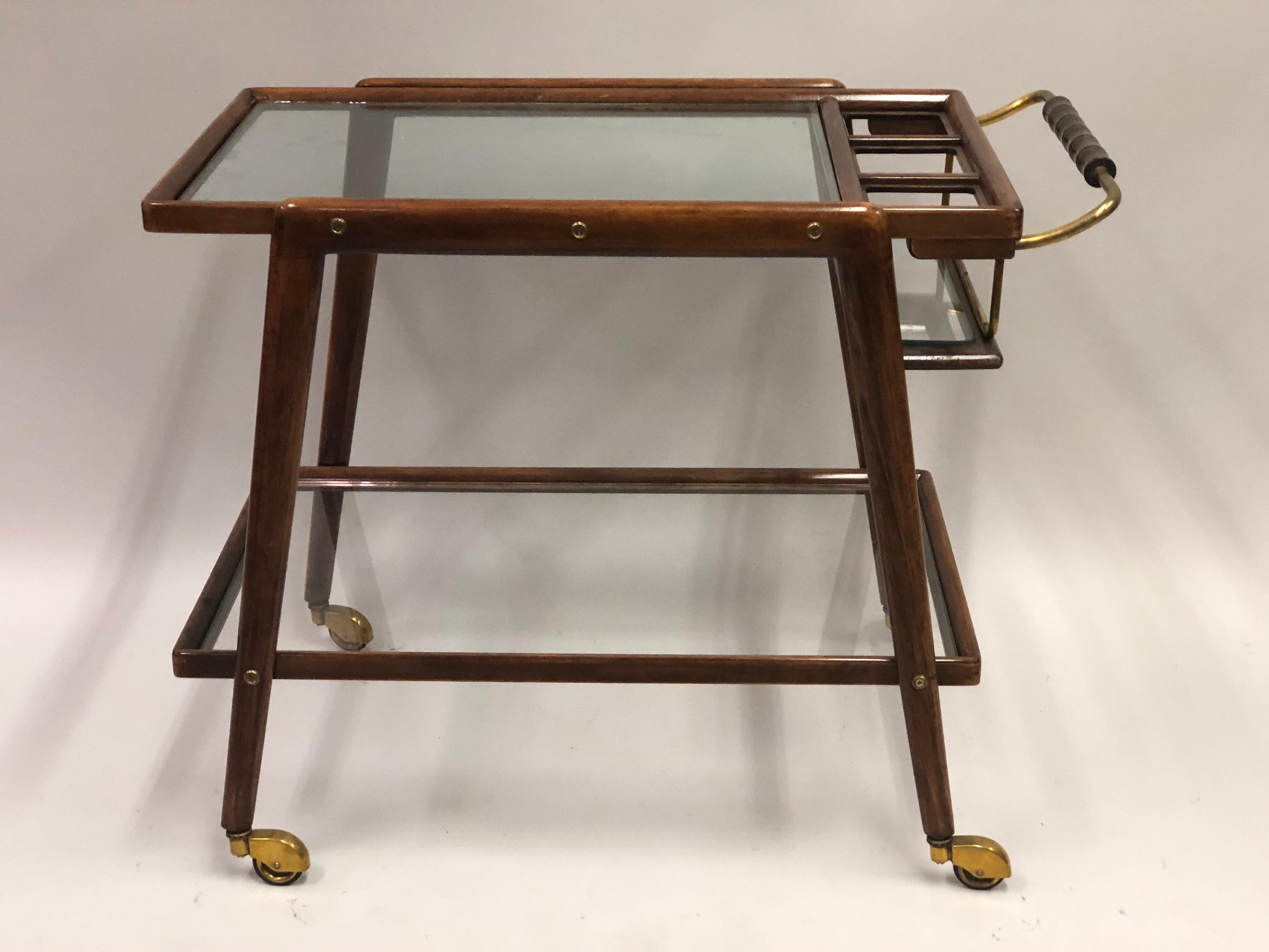 An elegant and stylish form.

Italian Mid-Century Modern bar cart in walnut wood with thick double level glass shelves and a separate bottle compartment for 3 bottles. A brass handle with carved wood grips completes the piece.

Solid brass