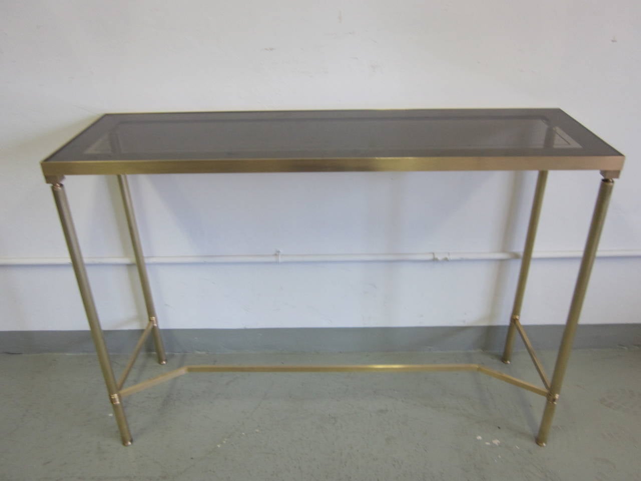 Sober, French Mid-Century Modern neoclassical console attributed to Maison Baguès in solid brass with a smoked glass top partially reverse painted to form a wide rectangular band in a muted grey around the edges.

References: Maison Jansen.