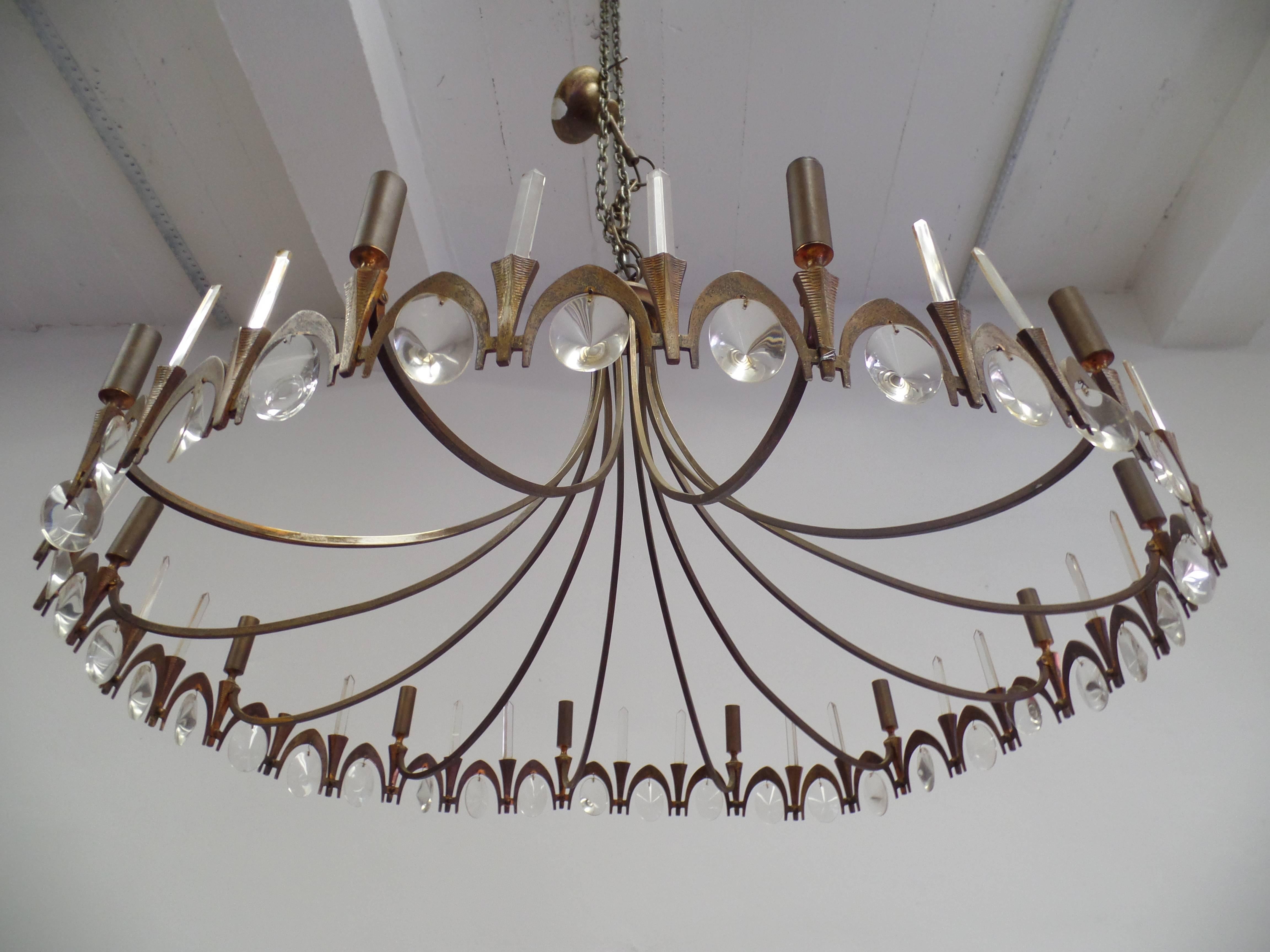 Elegant Italian Mid-Century gilt bronze and crystal chandelier in the Modern Neoclassical spirit.

The gilt bronze frame is arranged in a circle and composed of alternating sober torch forms and arch forms. The torches support candelabra sockets and