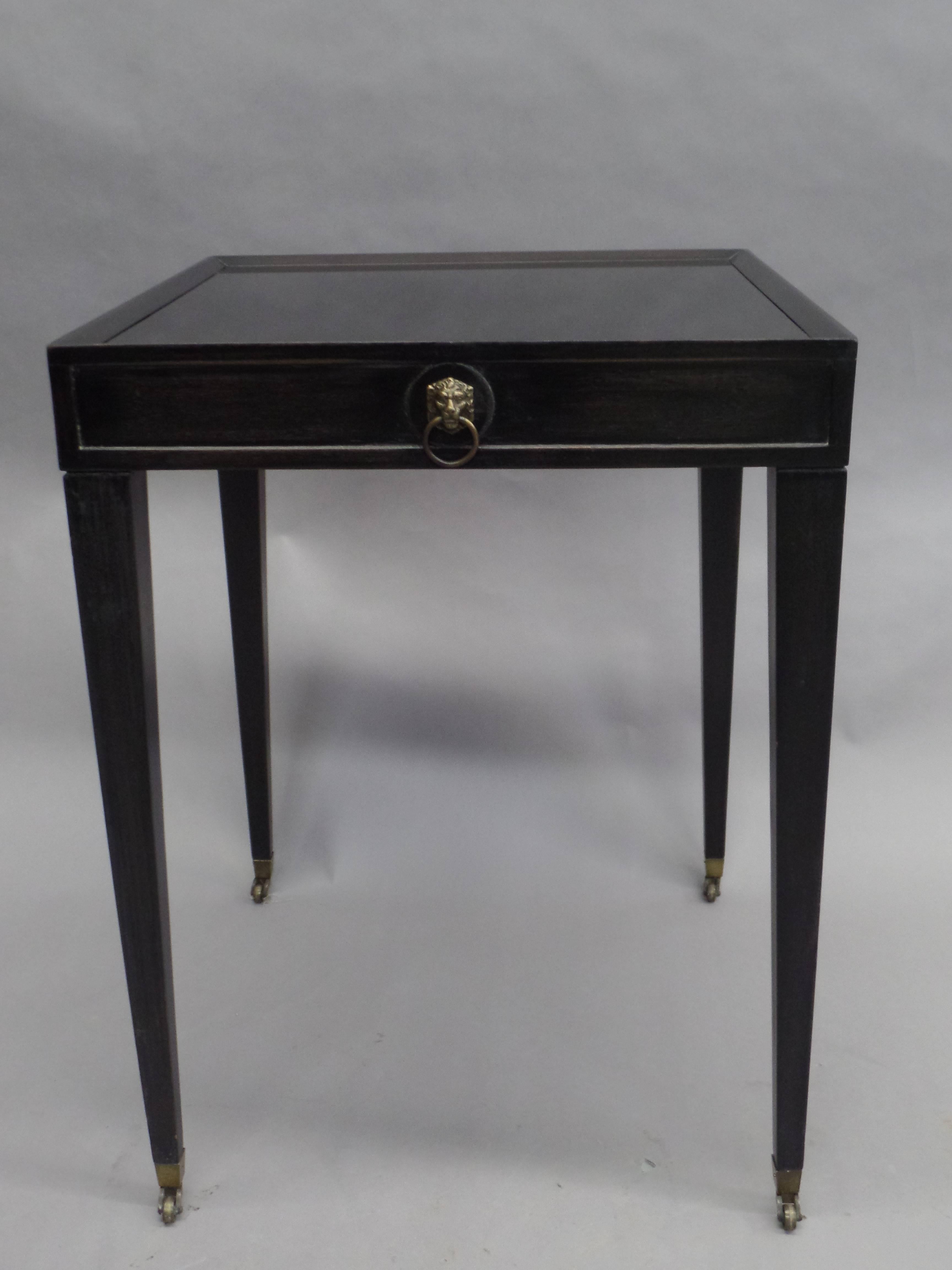 An elegant pair of French Mid-Century ebonized wood end tables / side tables in the modern neoclassical taste with chic tapered legs ending in brass sabots with brass wheels and featuring tops of black 'opaline' glass.

Literature: A similar model