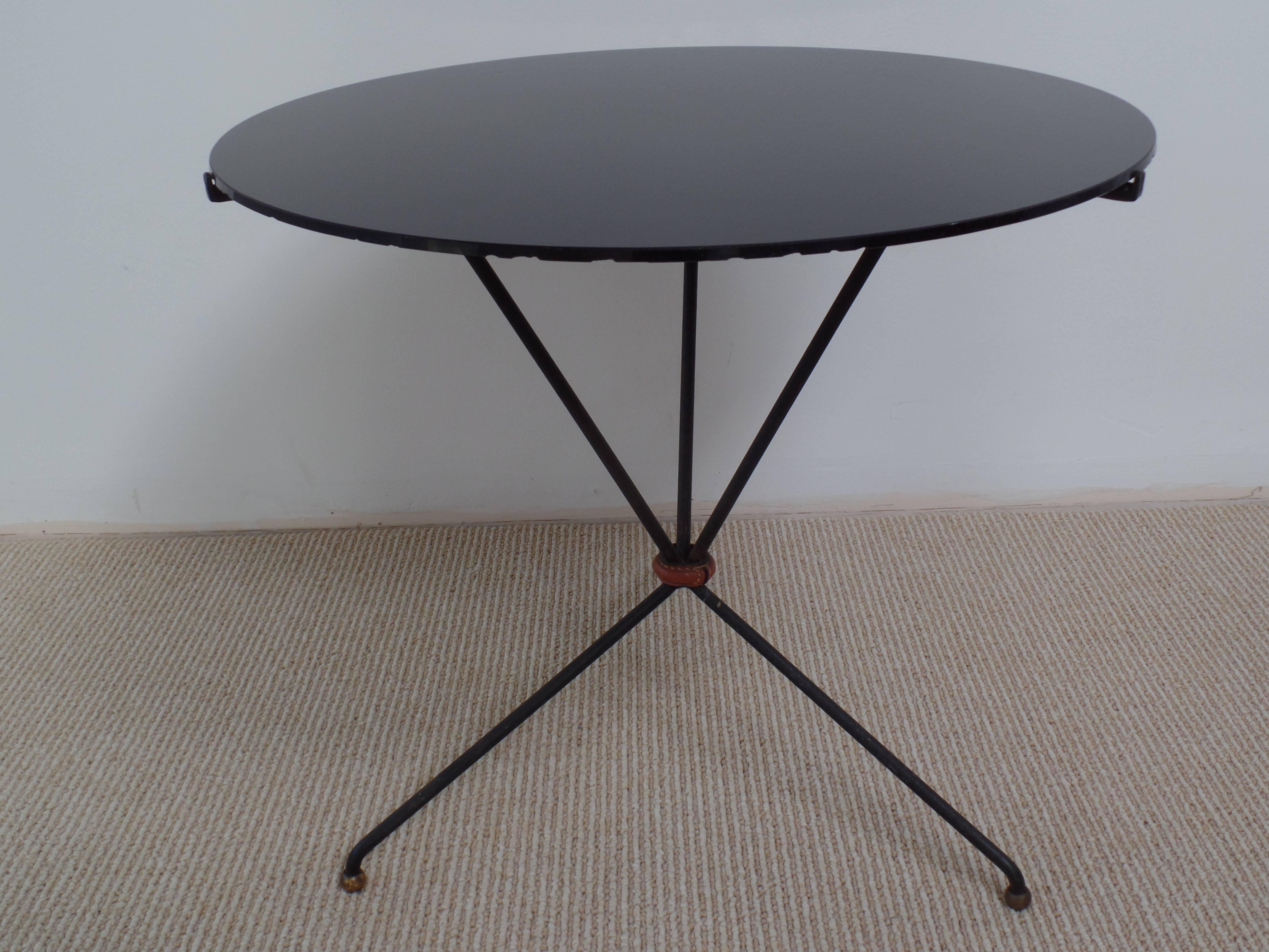 Elegant pair of end tables or Gueridons in the style of Jacques Adnet.

The tables are composed of wrought iron bases sitting on tripod legs ending in brass ball feet. The tabletop of black onyx glass rests on a tri-form supports with arched iron