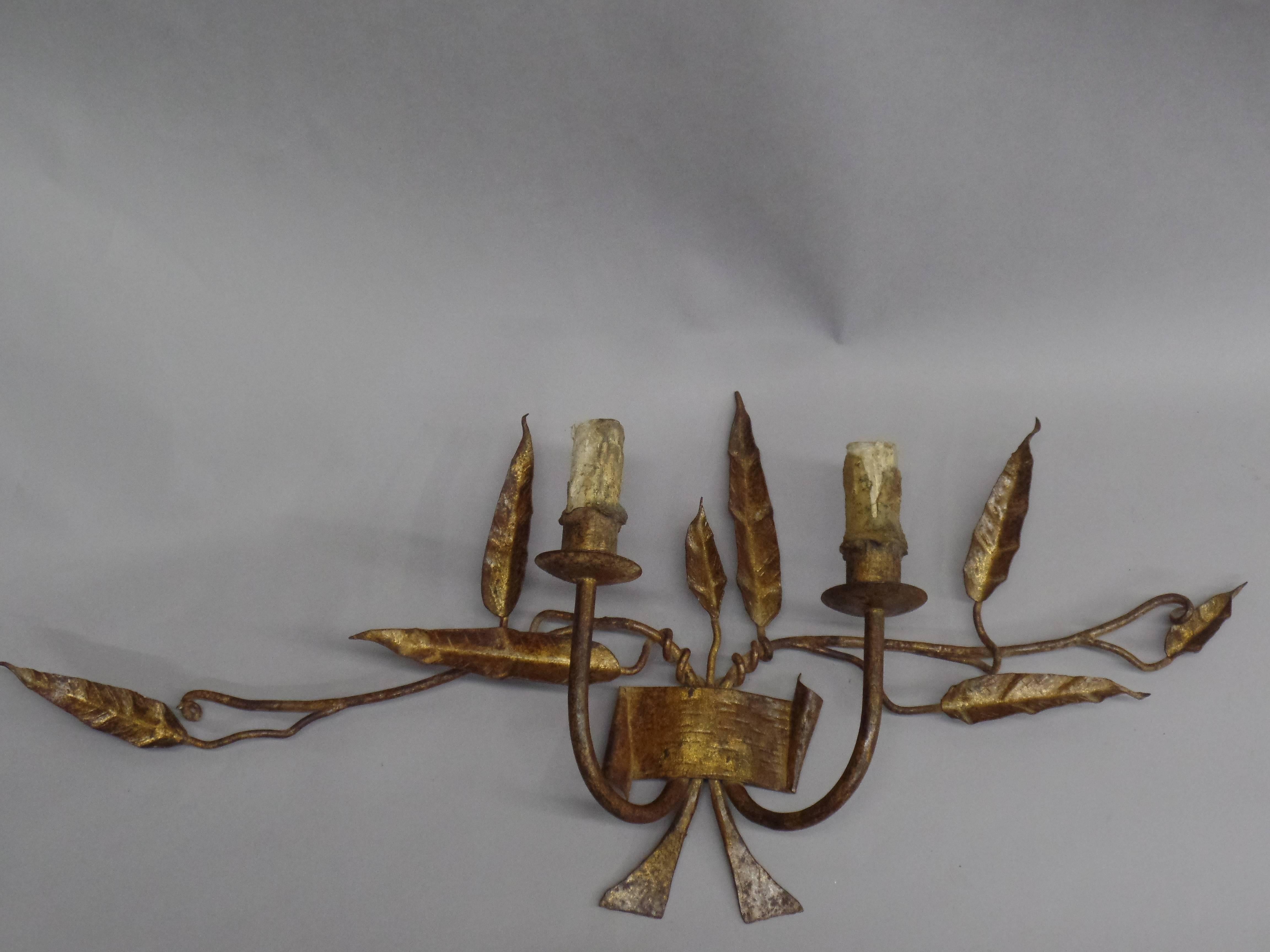 Exquisite pair of French 1940s hand-wrought iron and hand gilt double arm wall sconces. The pieces have a naturalistic, poetic quality conveying the sublime through its delicate branches and leaves. The artistry and delicacy of the pieces reflect