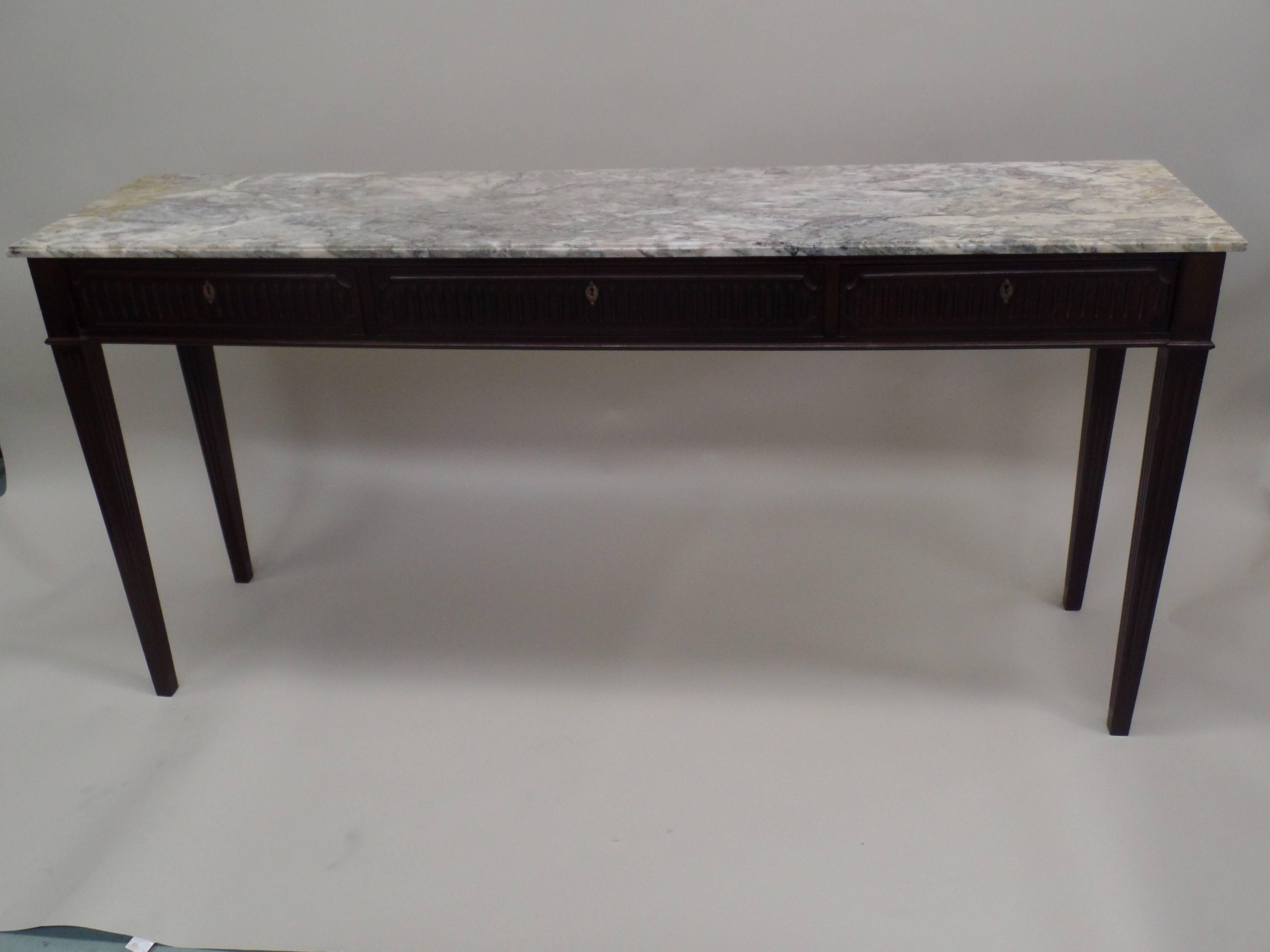 A large Italian Mid-Century console / sofa table with elegant form that embraces neoclassical tradition and modern sobriety. The legs are carved, fluted and tapered. The three-drawer fronts are carved and fluted to match. The original top of grey