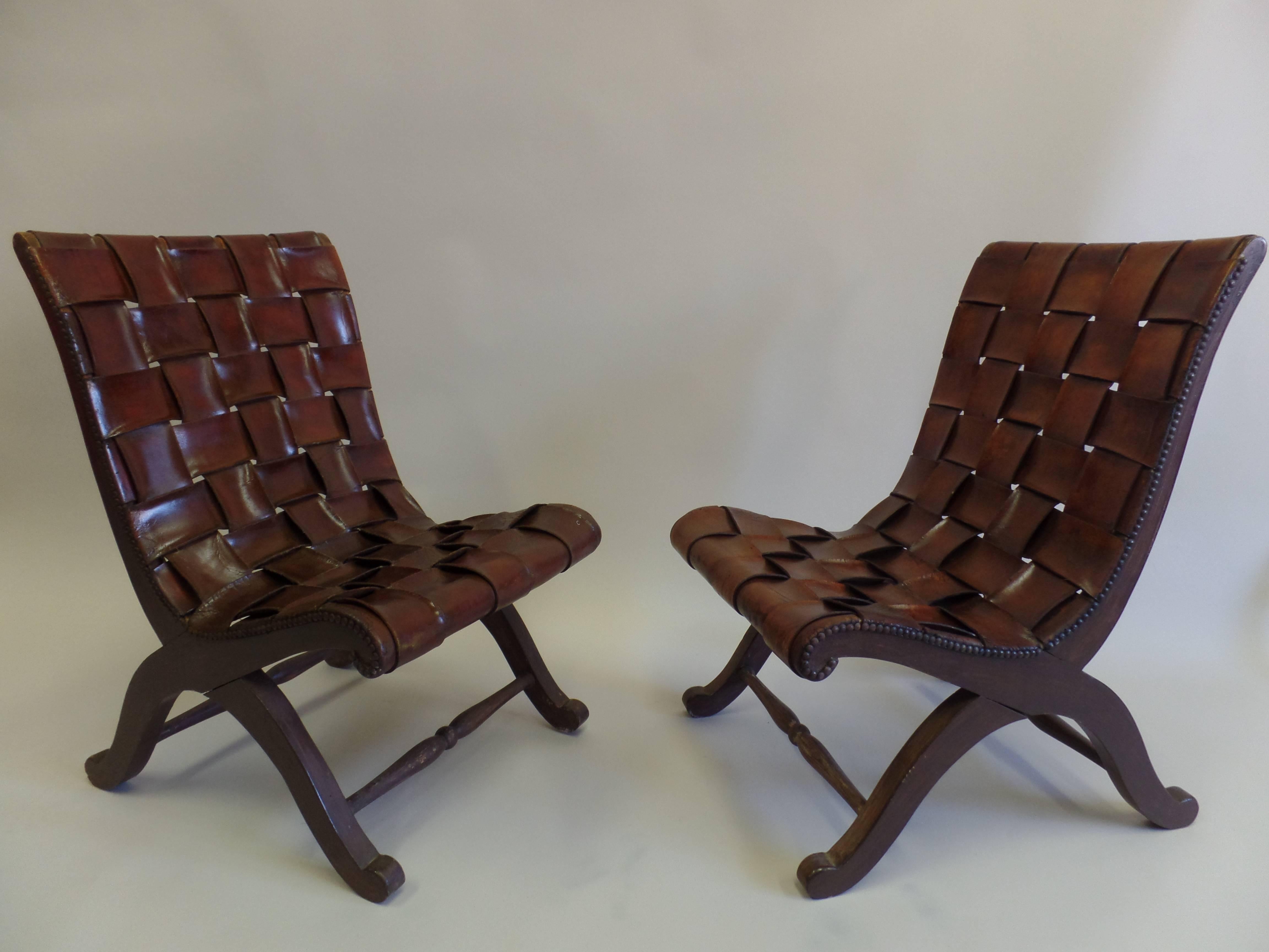 Elegant pair of slipper or lounge chairs with a neoclassical X-frame structure and upholstered with wide, thick cowhide leather straps with each piece inter-laced through each other. 

The leather is original and has a beautiful patina.
