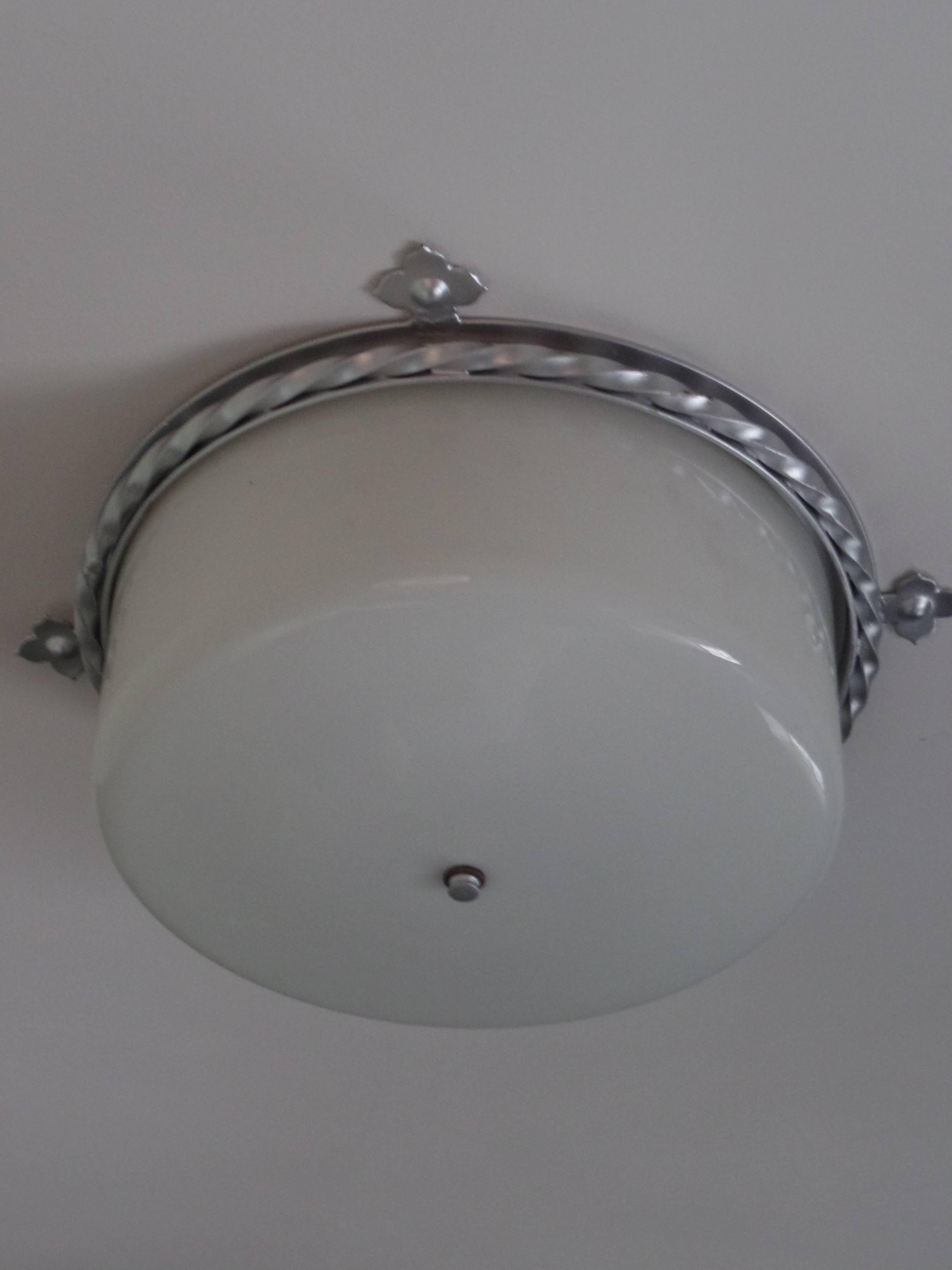 Elegant French mid-century flush mount ceiling lighting fixture composed of a silvered hand-wrought iron frame with an opaque thick milk glass reflector.

The frame is silvered and composed of twisted hand-wrought iron with four surrounding