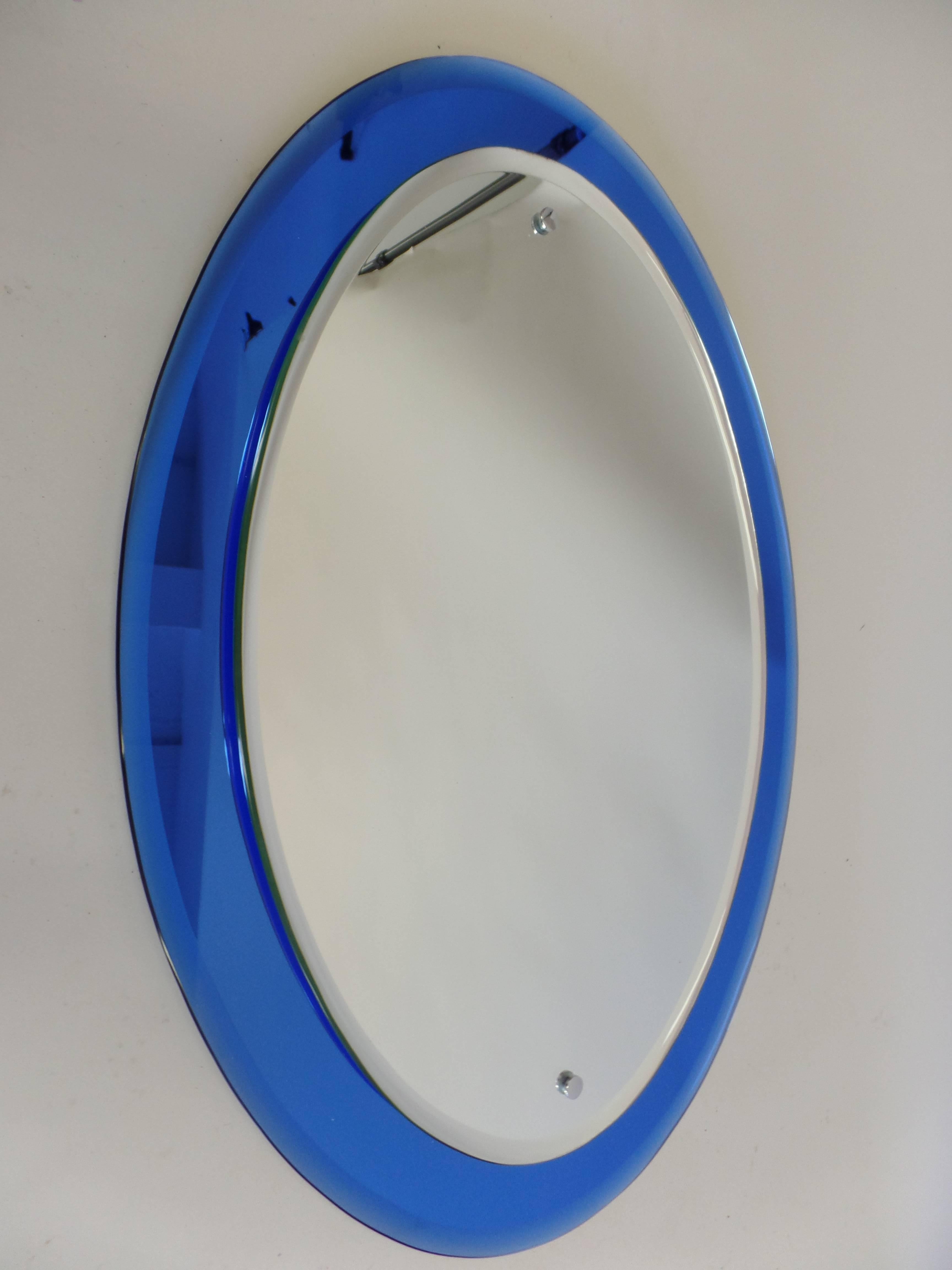 Elegant Italian Mid-Century Modern mirror in the style of Max Ingrand for Fontana Arte with a luminescent blue mirrored frame in an oval form.