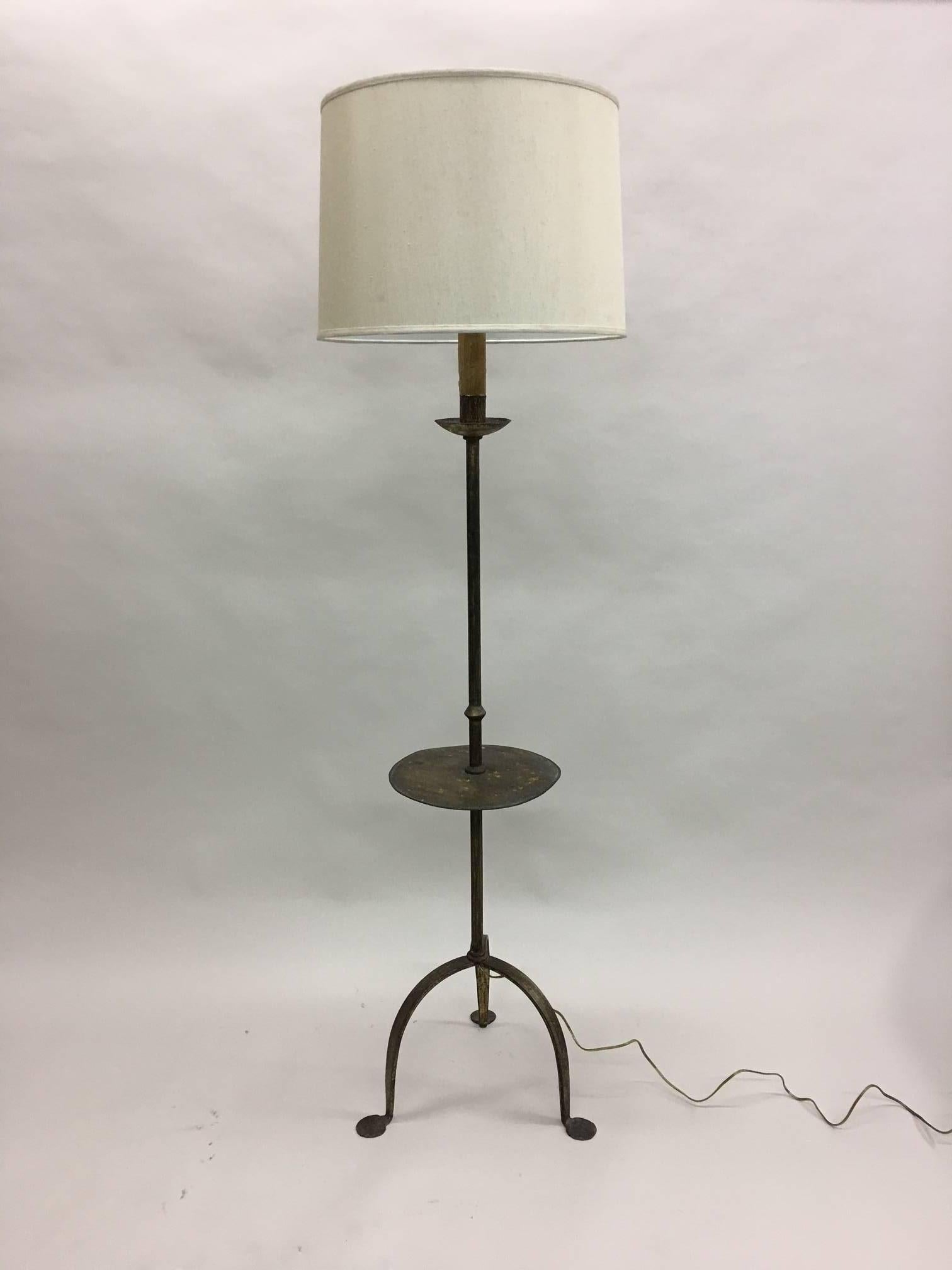 Stylish, elegant French, Mid-Century gilt iron standing lamp with an integrated circular side table. The piece features a tripod base with splayed feet. The gilt patina is gently worn.

Shade is for demonstration only. Shade dimensions are Top D: