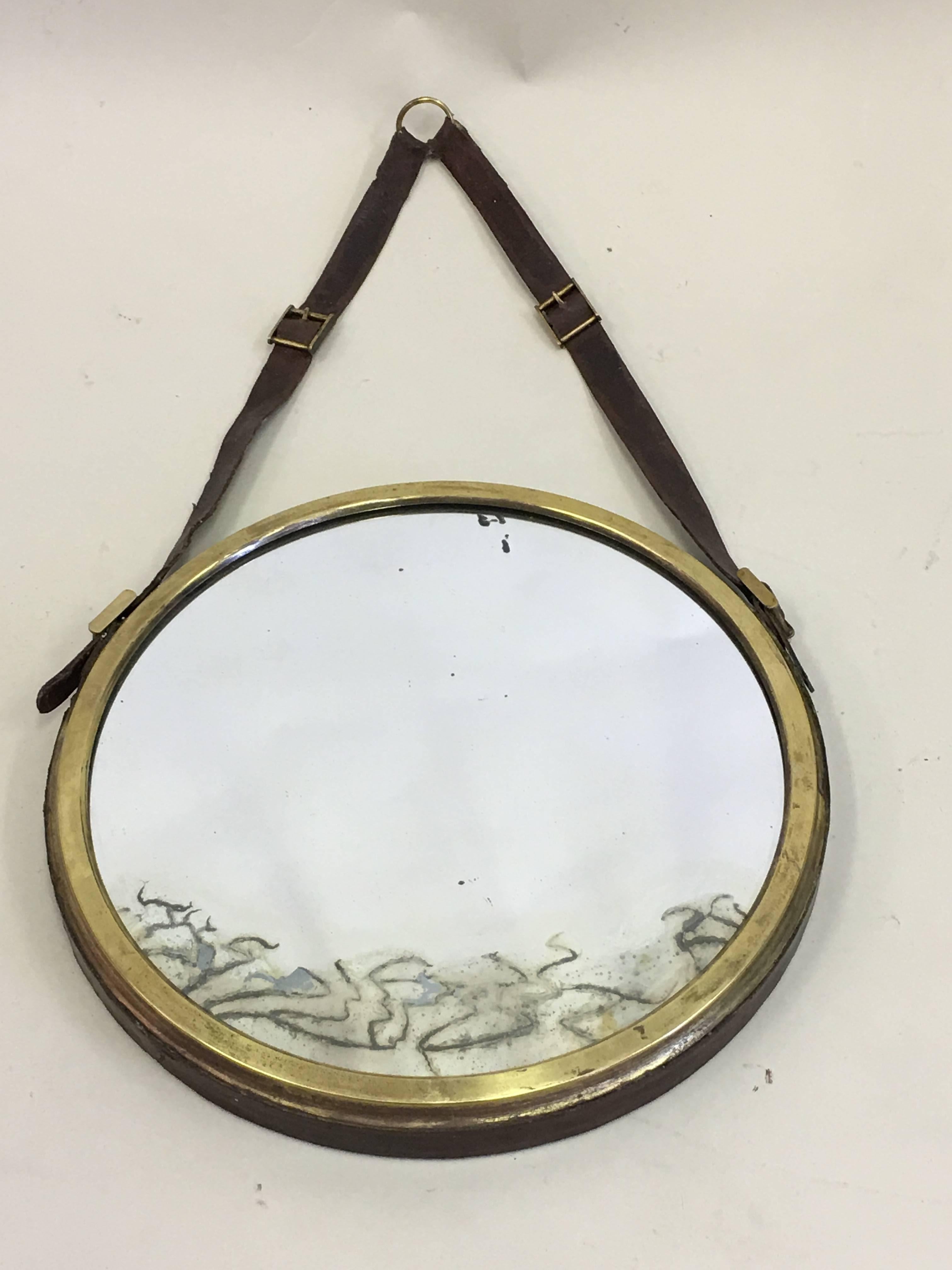 French Mid-Century Modern neoclassical leather wrapped mirror in the style of Jacques Adnet. The piece is round / circular with the frame in brass that has been covered in leather and suspended via leather straps.