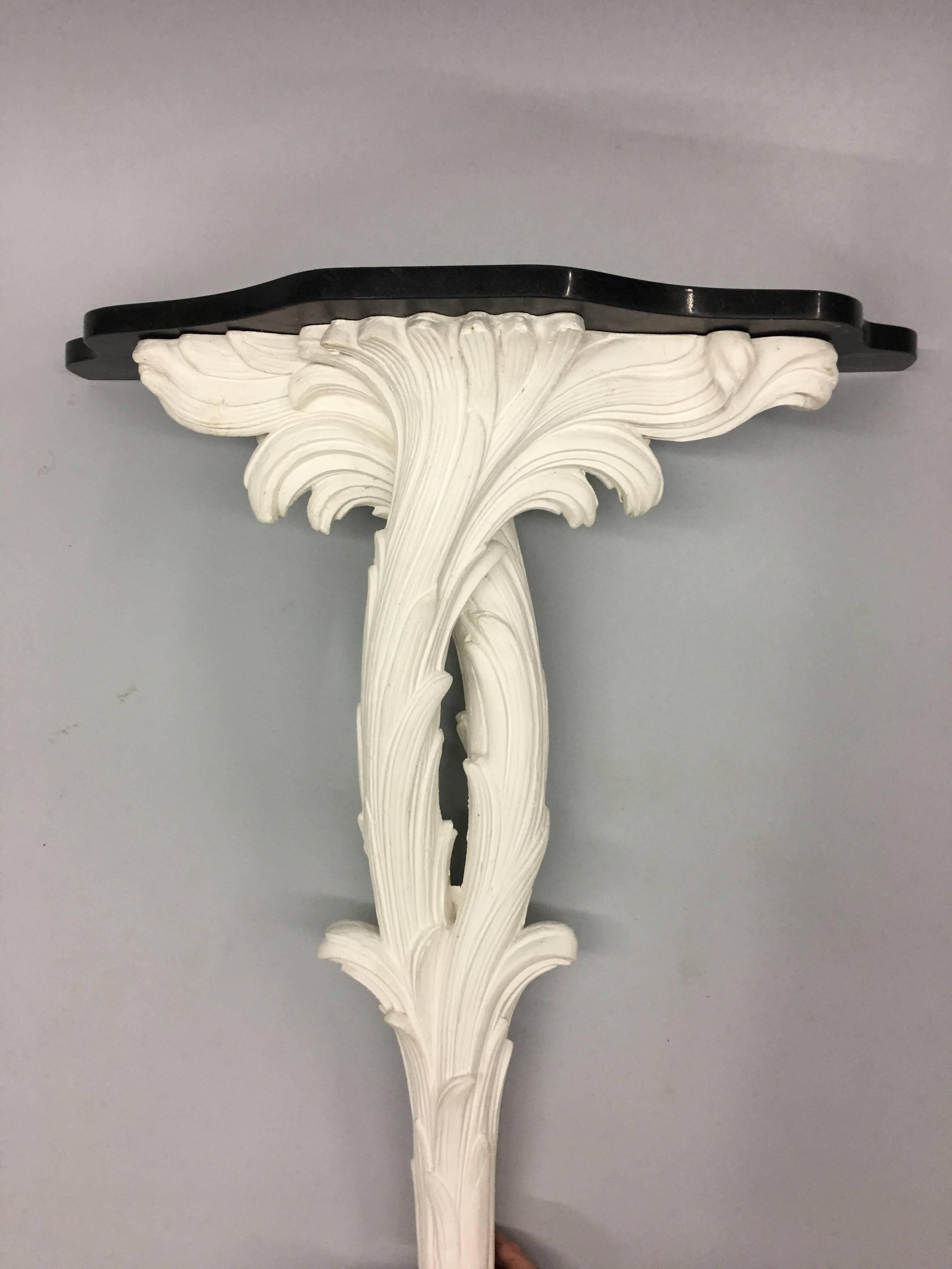 Two French plaster consoles in the unique Neo-Baroque / late Art Deco / early Mid-Century Modern style of Serge Roche. The stem and base are formed in plaster by elegant and lush palm frond decoration.

The pieces are finished by black stone tops in