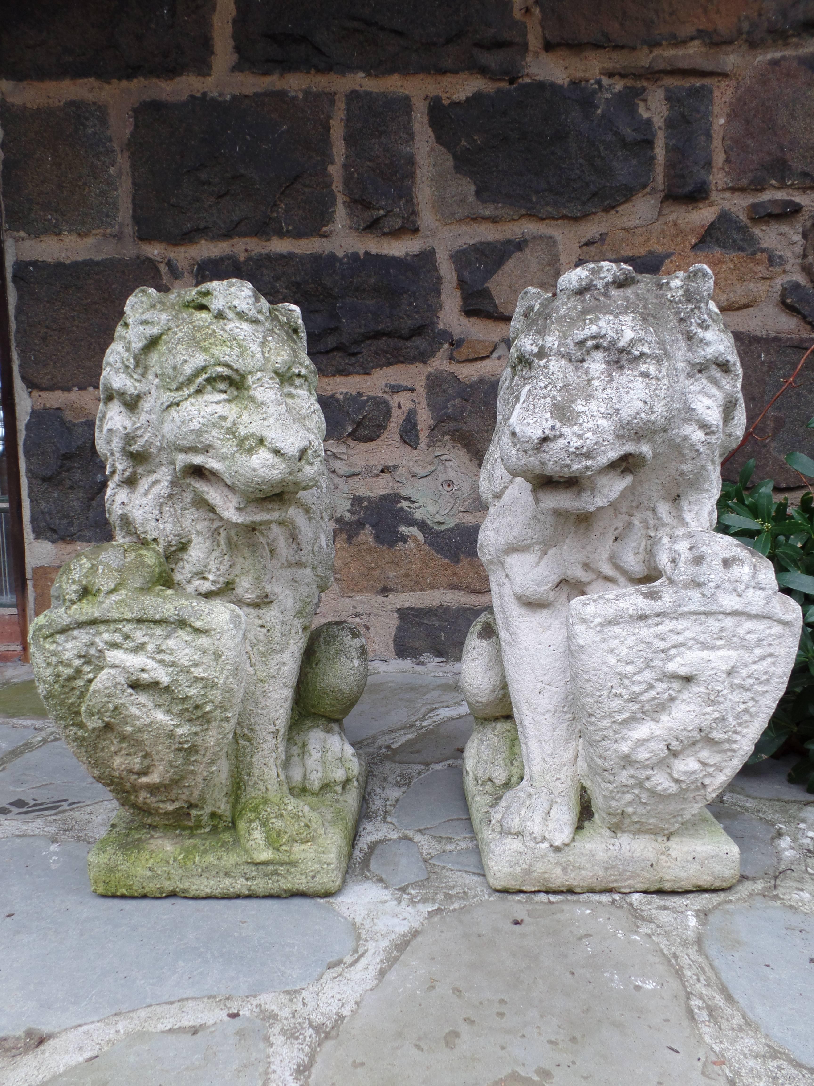 Pair of French 19th century garden statues of hand-carved stone lions with shields. 

Each is crouched on their hind legs with an arm supporting an escucheon or shield upon which is cut a family coat of arms reflecting noble 18th century