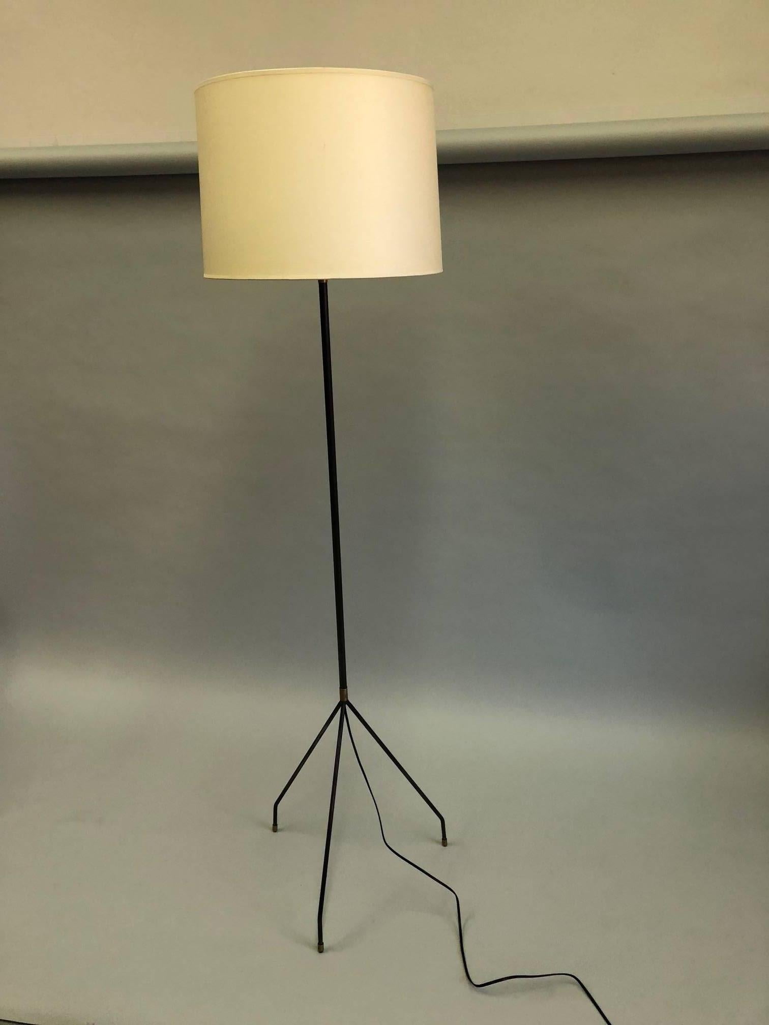Elegant, sleek pair of French Midcentury Modern hand wrought iron floor lamps by Disderot. The standing lamps are delicately conceived with a slender iron stem that parts into a tripod base composed of thin, round iron bars that narrow to slim feet.