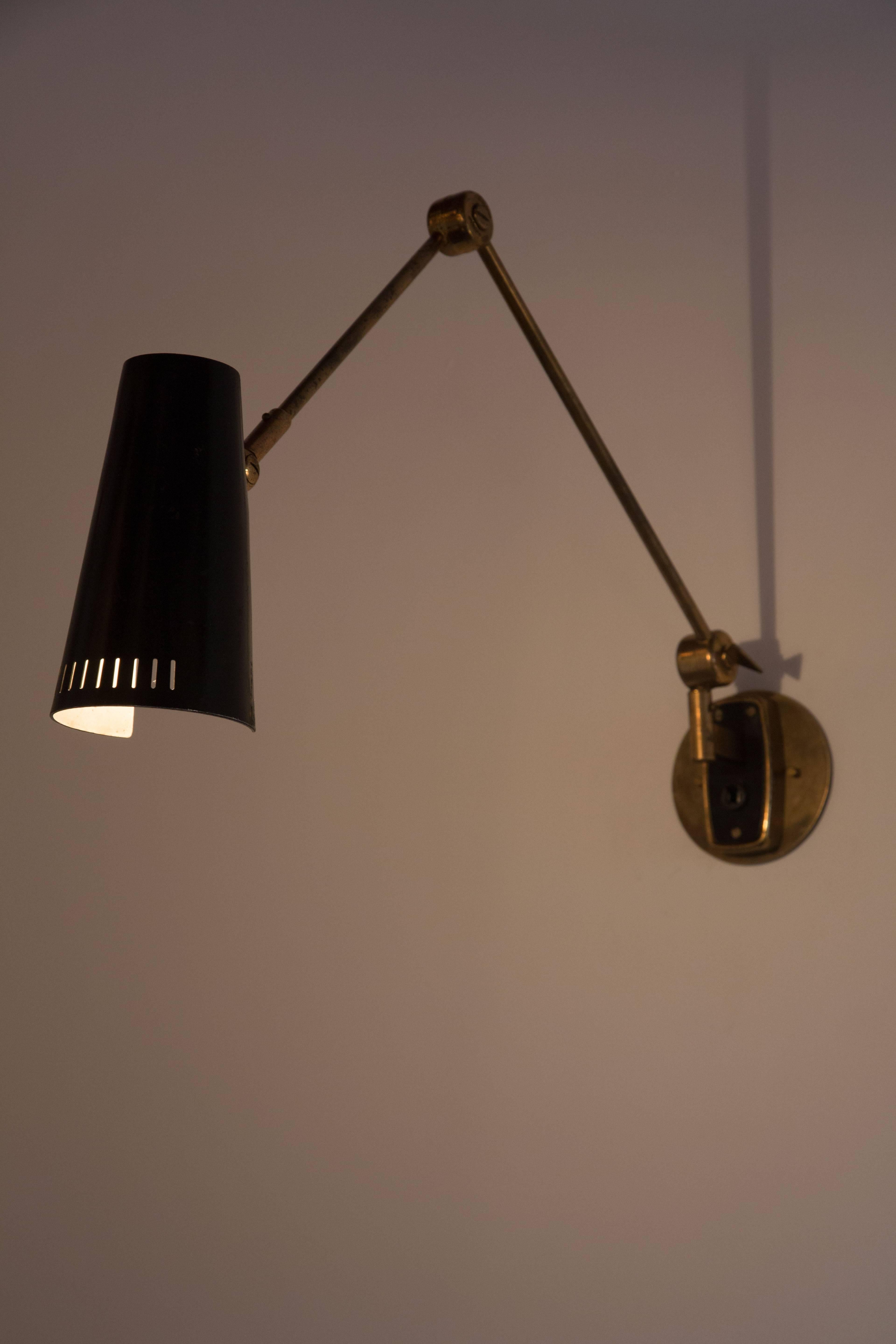 Brass wall light, painted metal shade with vertical perforations at the base. Arm of light articulates up/down by adjusting the key. Shade articulates up/down by adjusting the joint at base of shade. Arm pivots left to right. Original on/off switch