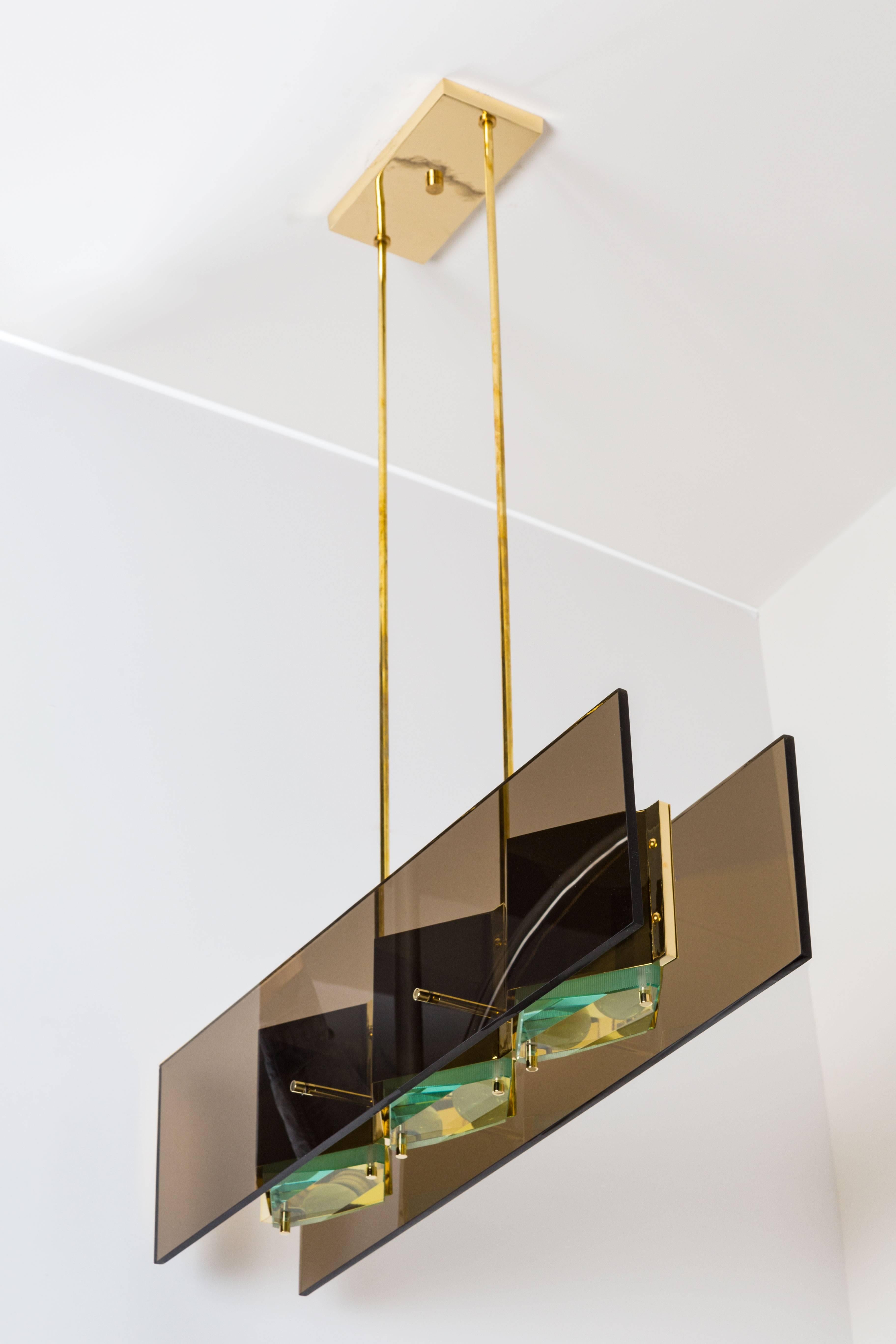Rare 1960s Stilnovo brass chandelier with diamond cut green glass 
diffusers. Two smoked glass rectangles frame the brass shades.
Fully restored with proof of original label. Green glass diffusers and canopy are replaced.
Lampage is three E27
