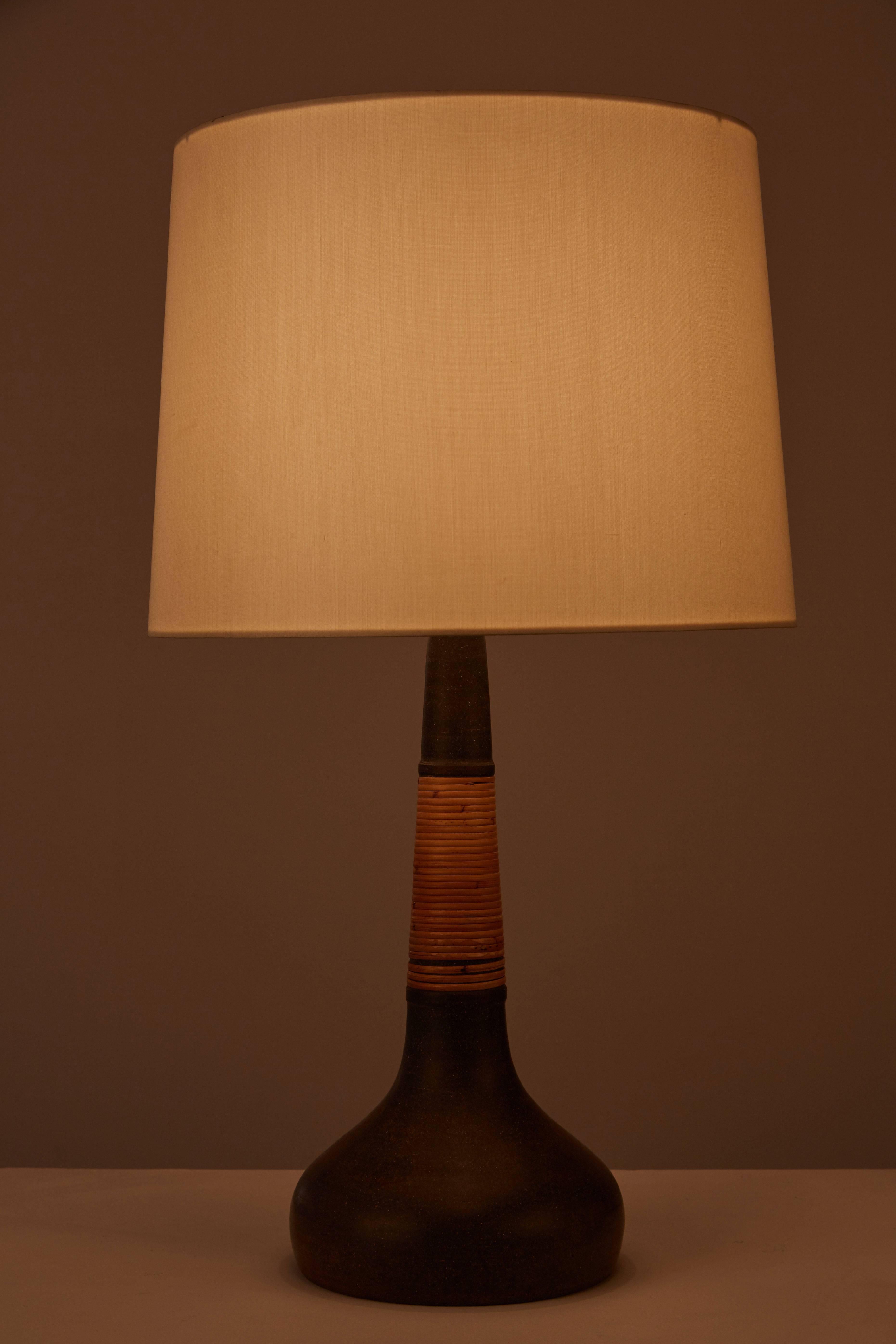 Two table lamps with round base and long tapering neck in deep brown stoneware with rattan wrapping. Custom silk shade. Made in Denmark in the 1960s. Retains Incised “HAK” and “Le Klint” on bottom of light. Takes an E27 60w maximum bulb. Priced