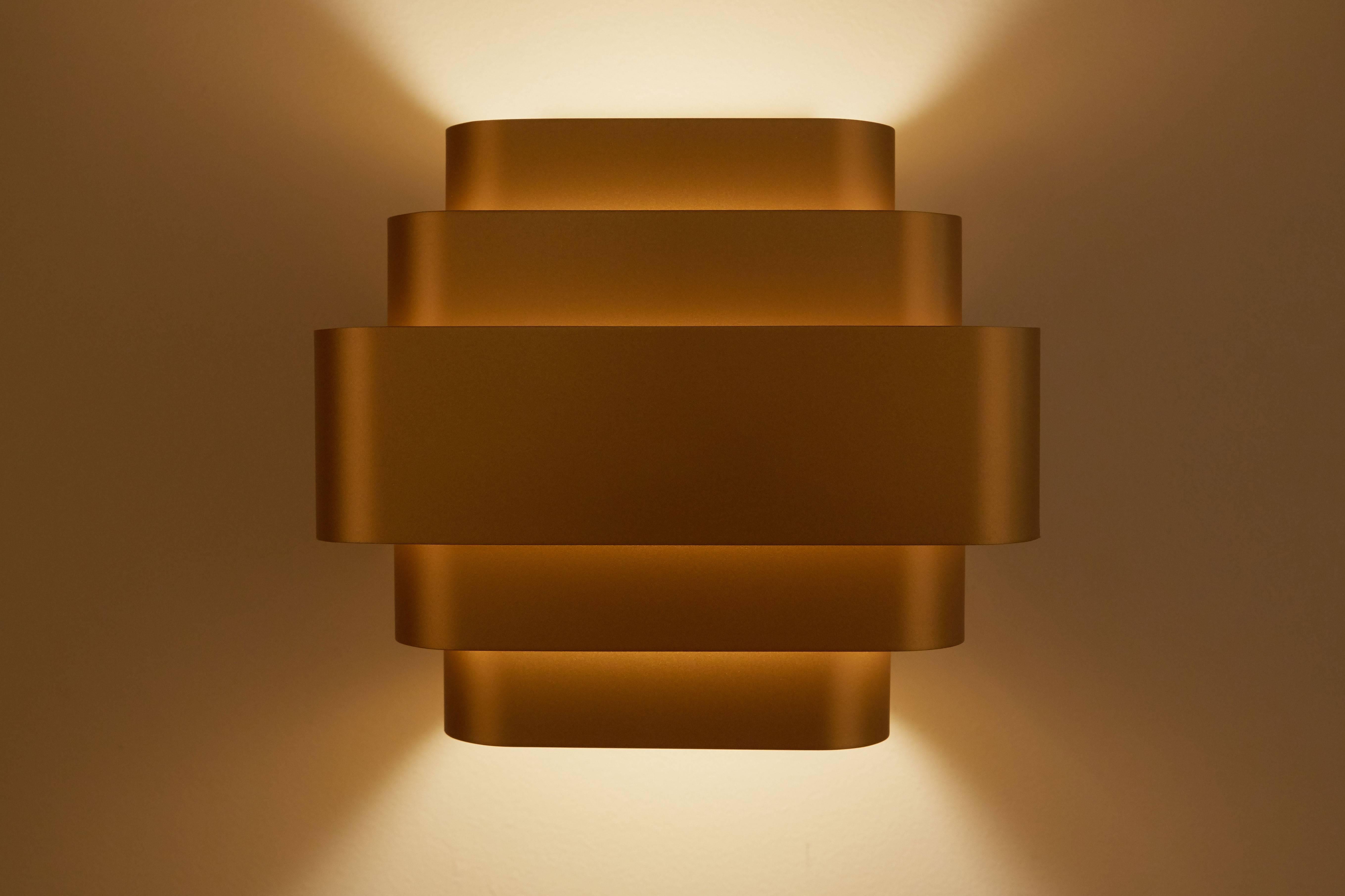 Brass sconces originally designed by Jules Wabbes, circa 1960s. These current productions are manufactured in Belgium. Made from anodized brass colored gilt aluminium. The five anodized aluminum strips provide diffused light at top and bottom. Wired