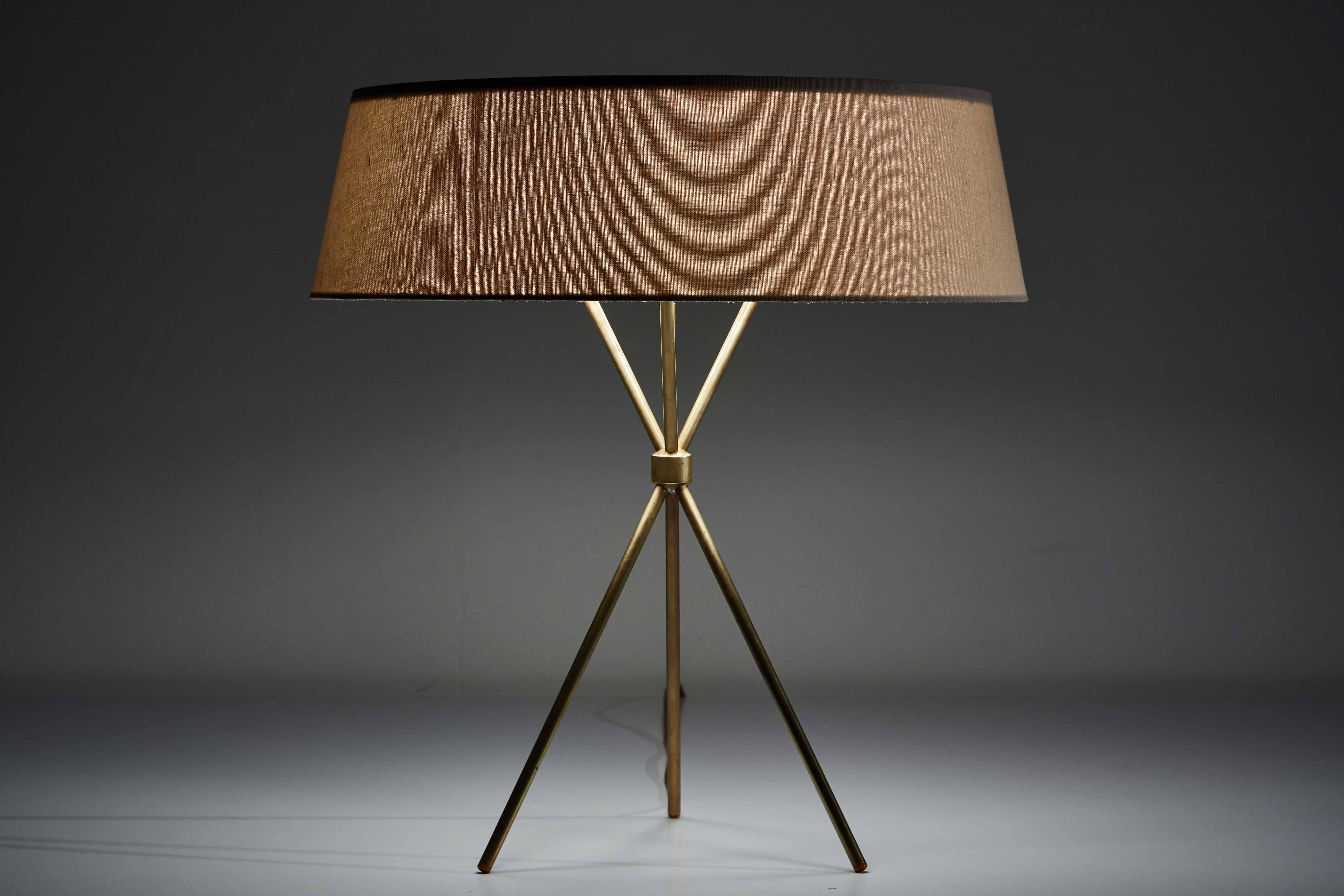 Tripod table lamp designed by T.H. Robsjohn-Gibbings in the US circa 1950s. Manufactured by Hansen. Brass legs and hardware with custom linen shade. Retains original manufacturer's stamp. Original cord. Takes one E26 100w maximum bulb.