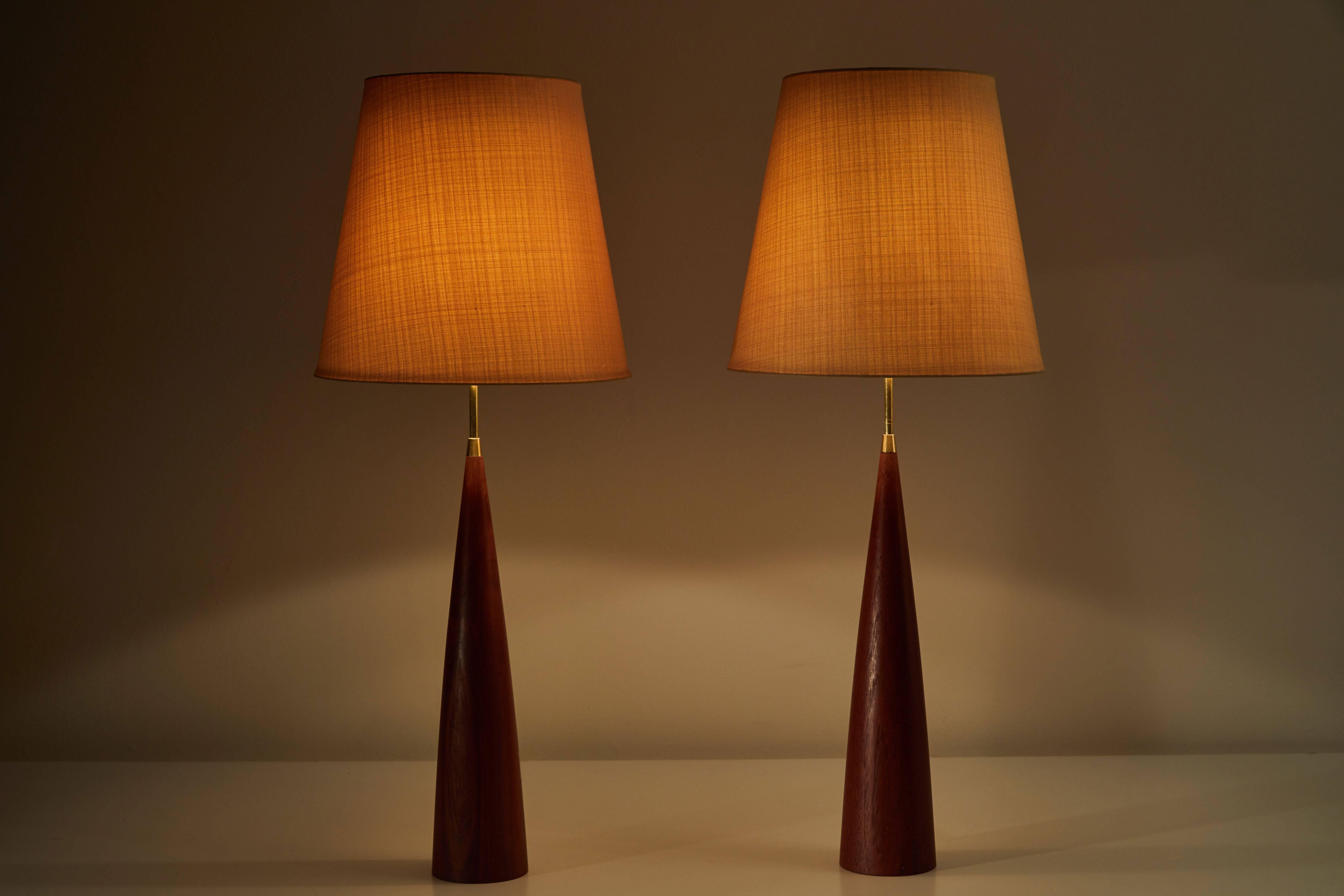Pair of teak table lamps with original linen shades and brass hardware designed in Sweden, circa 1950s. Original cords. Each light takes one E27 100w maximum bulb.