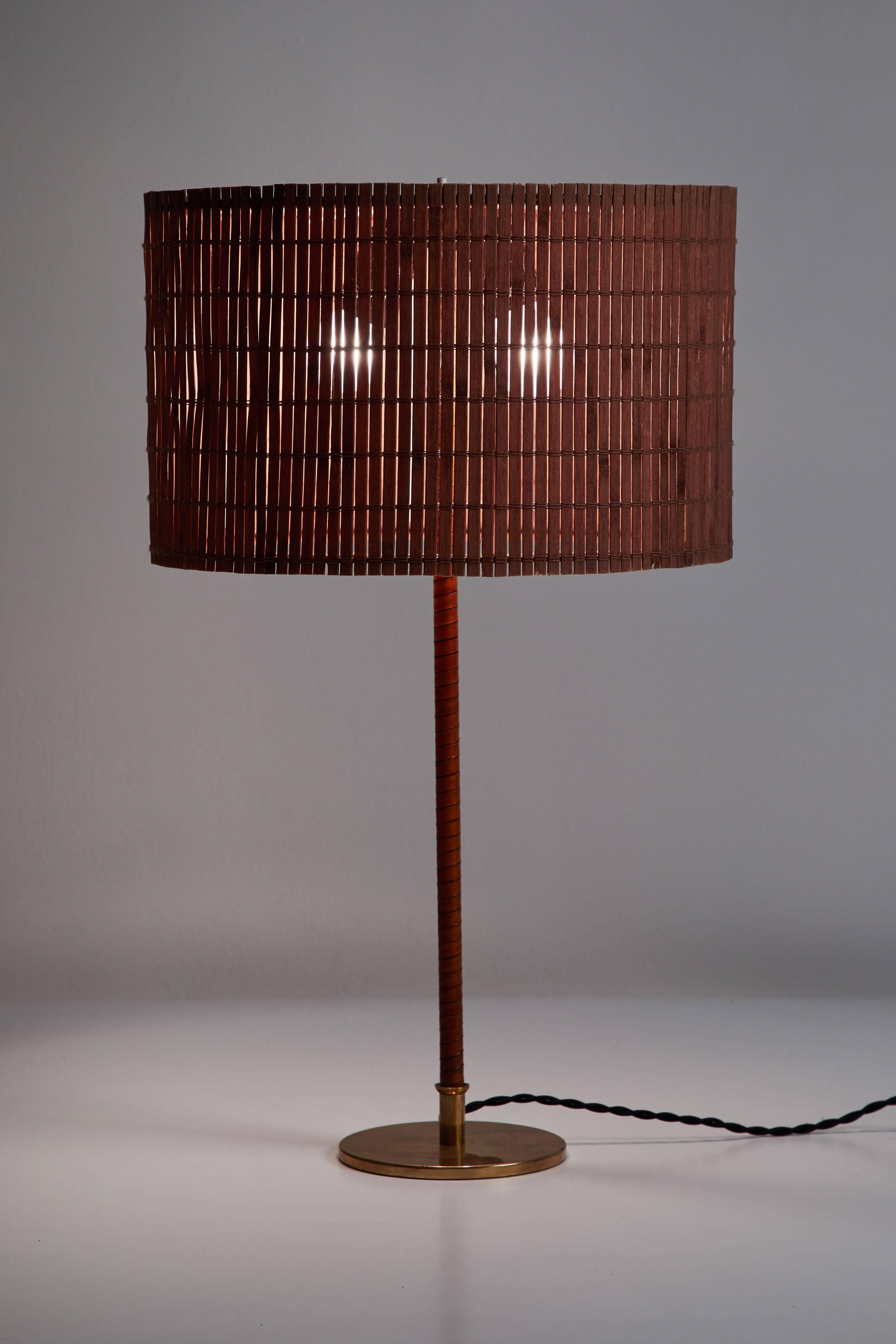 Model 9205 table lamp by Paavo Tynell for Taito Oy designed and manufactured in Finland, circa 1950s. Brass stem wrapped with leather, cane shade. Rewired with French twist silk cord. Takes one E27 75w maximum bulb.