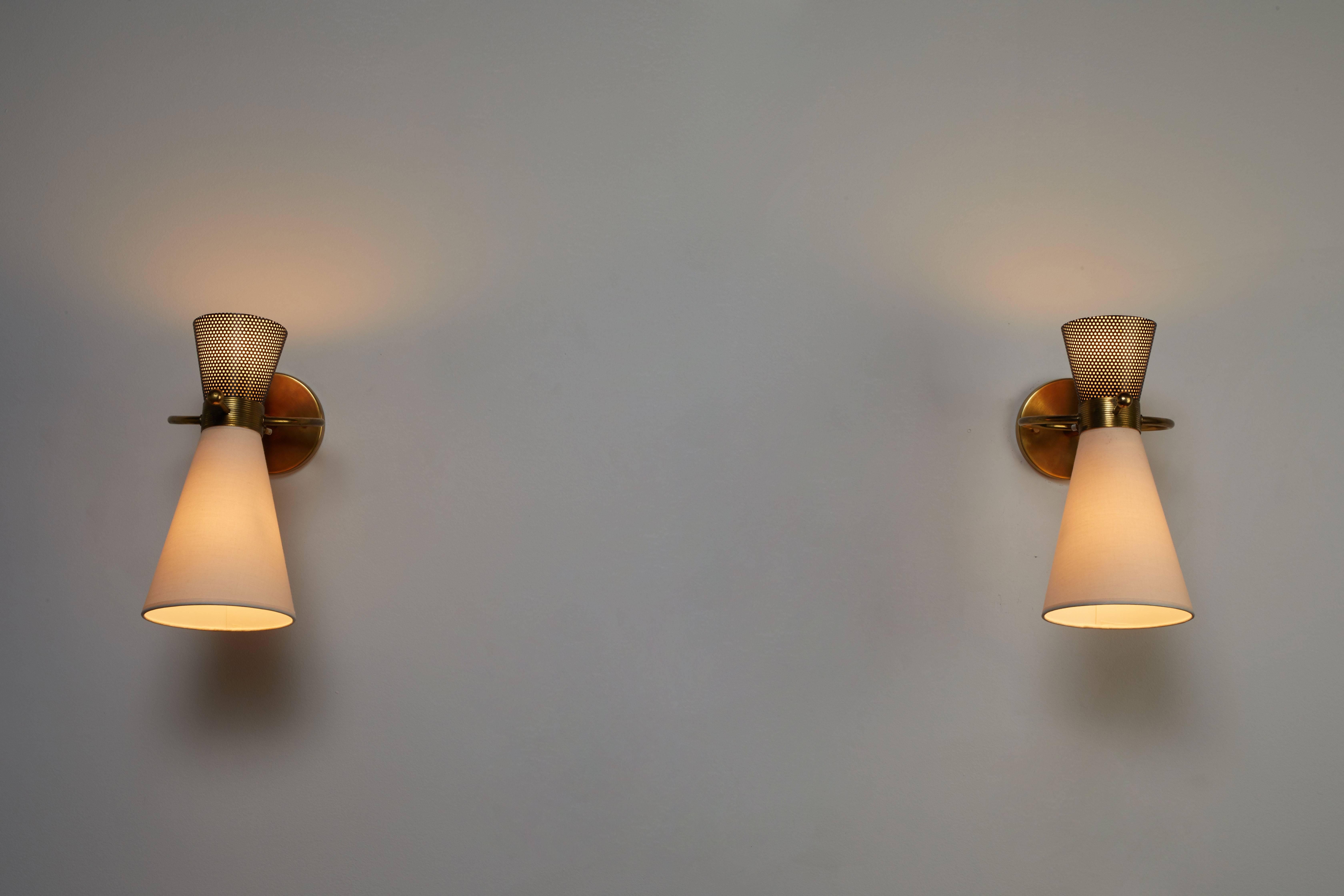 Pair of sconces by Maison Arlus manufactured in France, circa 1950s. Perforated enameled metal, silk shades and brass hardware. Sconces pivot up/down and left/right. Wired for US junction boxes. Each sconce takes one 60w bayonet bulb.