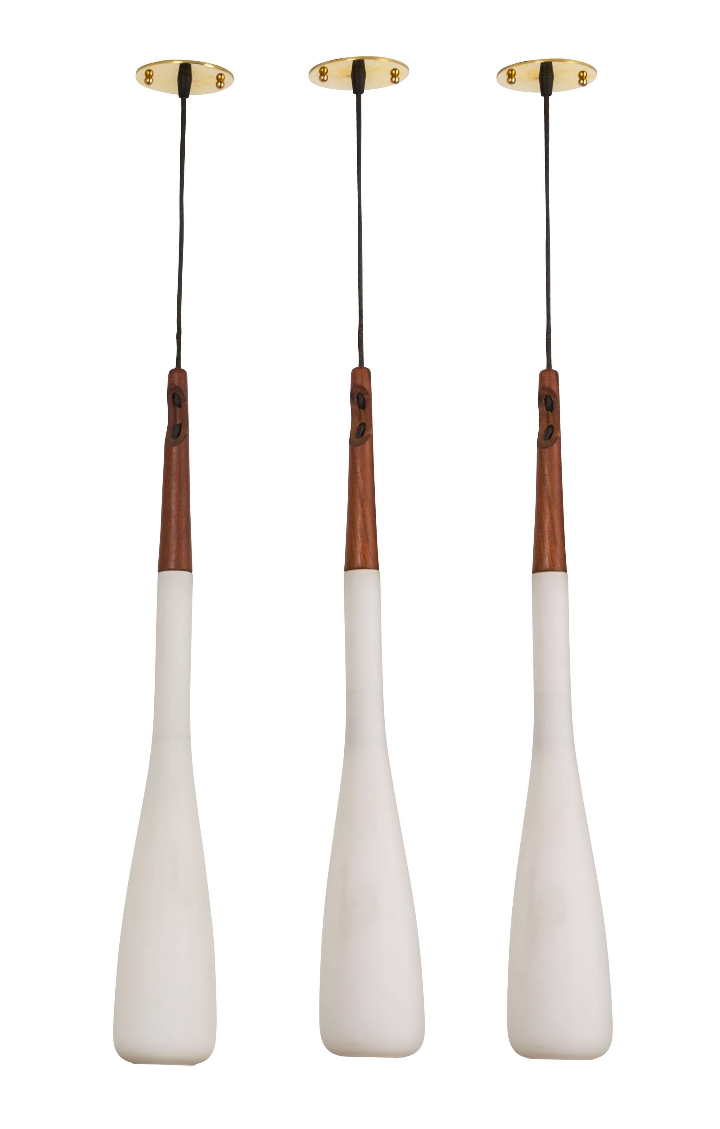 Molded white brushed satin glass pendants with teak stems designed by Uno & Osten Kristiansson. Custom backplates and original cloth cords. Priced to be sold individually. Overall drop can be customized. Each pendant takes an E27 40w maximum bulb.
