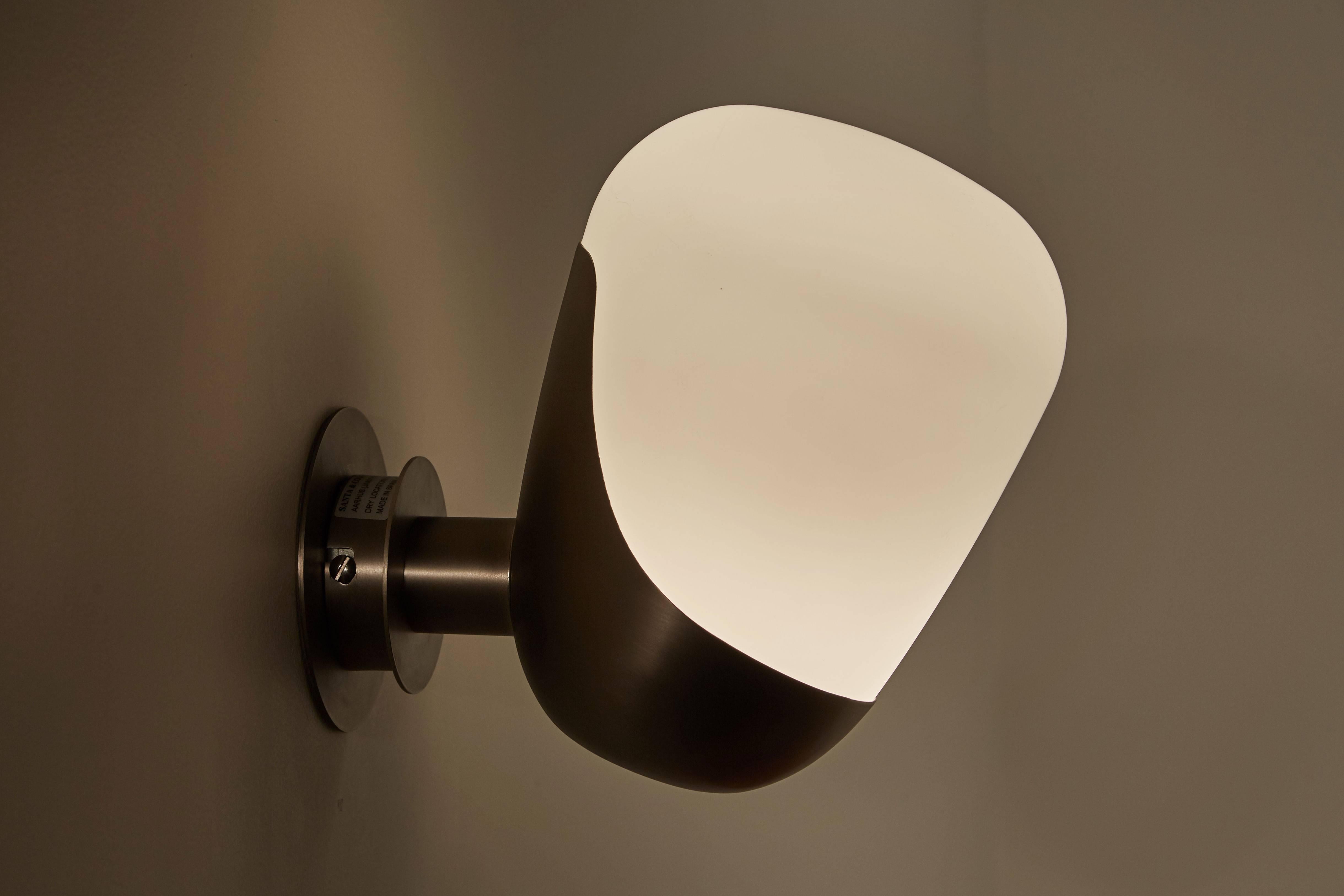 The Aarhus sconce was originally designed in 1946 by Arne Jacobsen and Erik Moller. This Santa & Cole Aarhus re-edition of the Classic sconce features an angled white opal glass shade in a satin nickel metal base. Manufactured in Spain. Wired for US