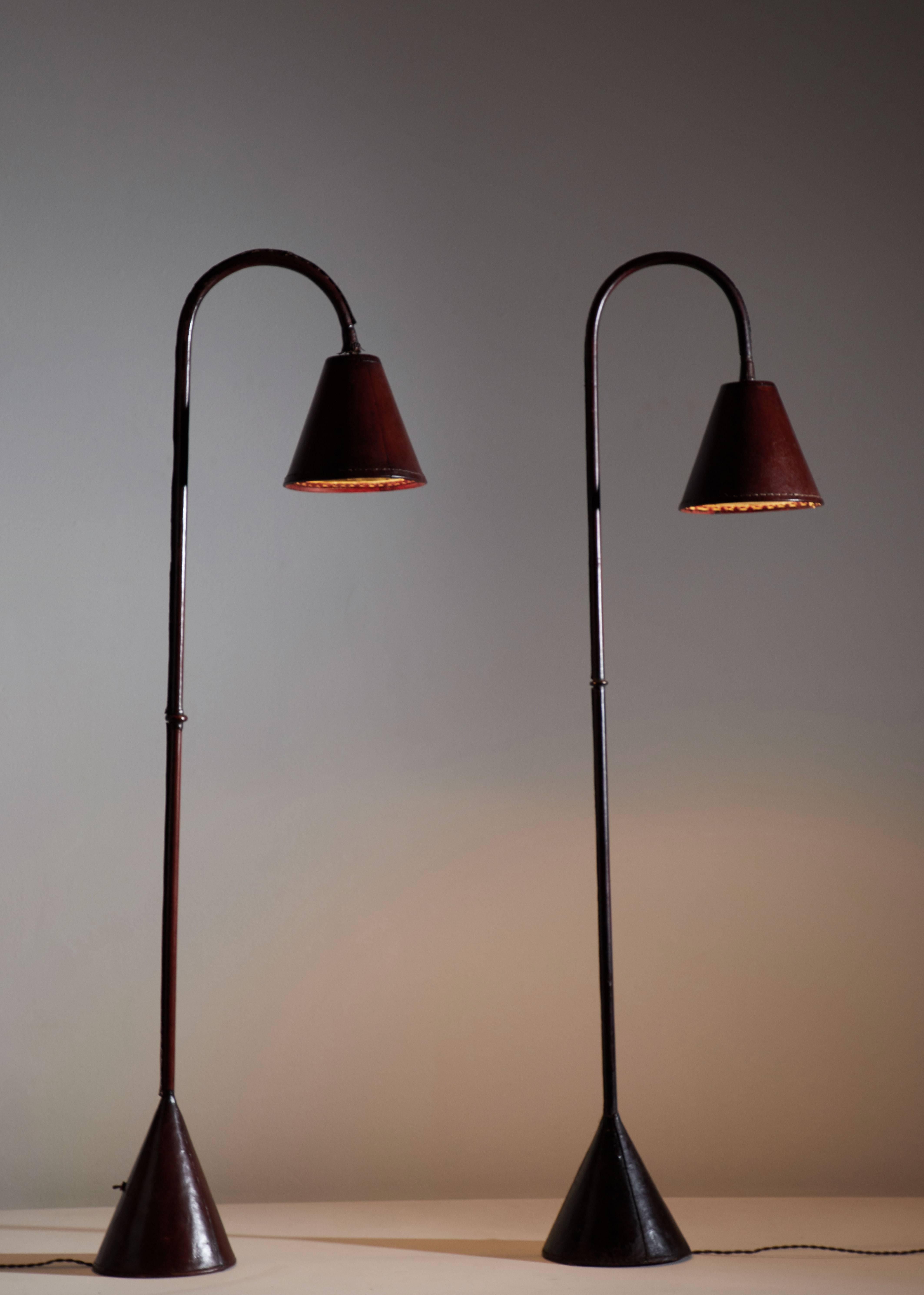 Spanish Leather wrapped floor lamp in the Style of Jacques Adnet designed in France, circa 1950s.
Saddle-stitched Mahogany leather over steel. Shade articulates up/down and left/right. On/off switch on base of lamp. Rewired with French twist cord.