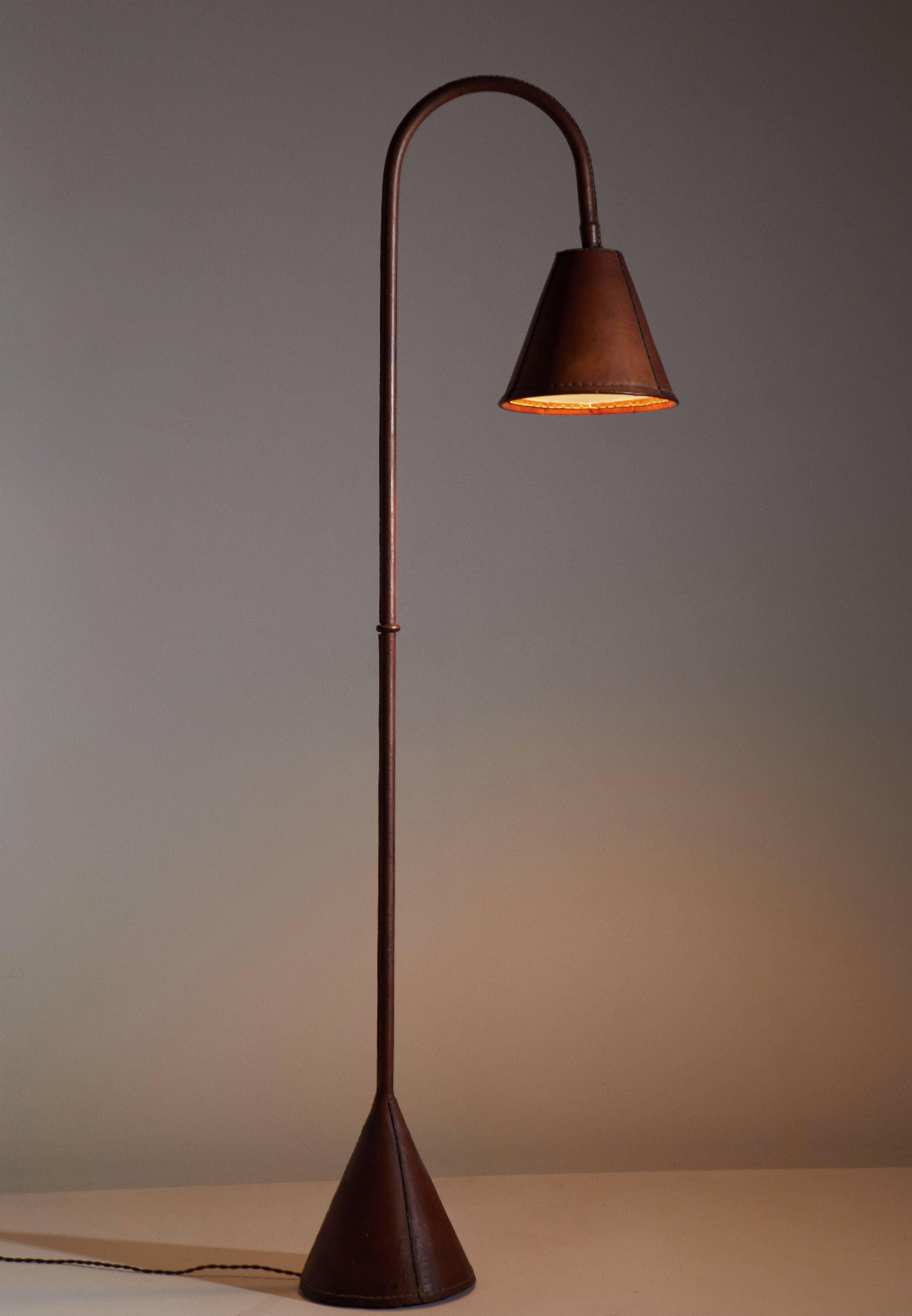 Spanish Leather wrapped floor lamp in the style of Jacques Adnet designed in France, circa 1950s.
Saddle-stitched leather over steel. Shade articulates up/down and left/right. On/off switch on base of lamp. Rewired with French twist cord. Original