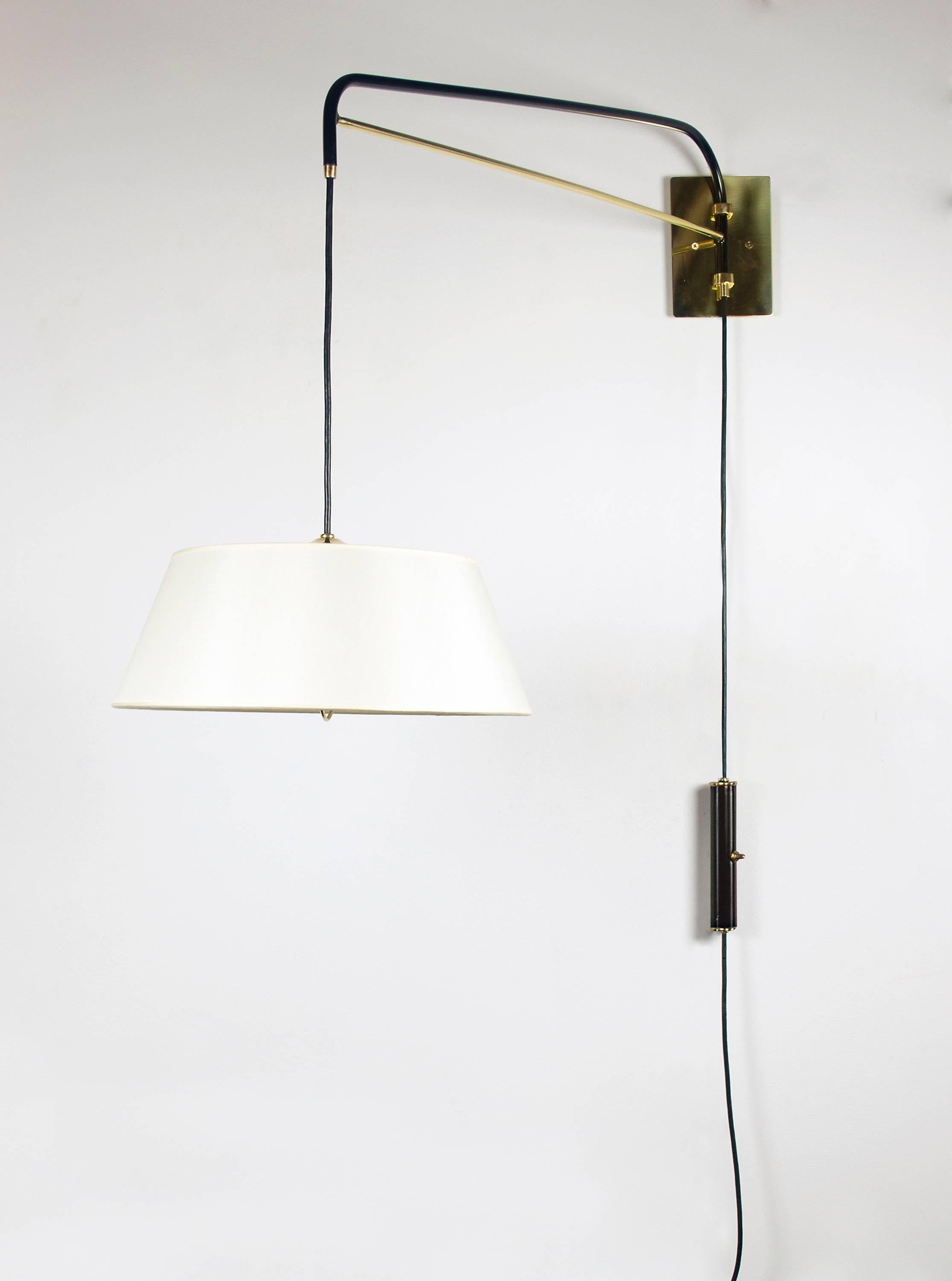 Two graceful wall sconces which are handcrafted with a black enamel finish and polished brass. An elegant linen shade diffuses a soft light. This fixture is adjustable, the switched counter weight system allow for height adjustments while the arm