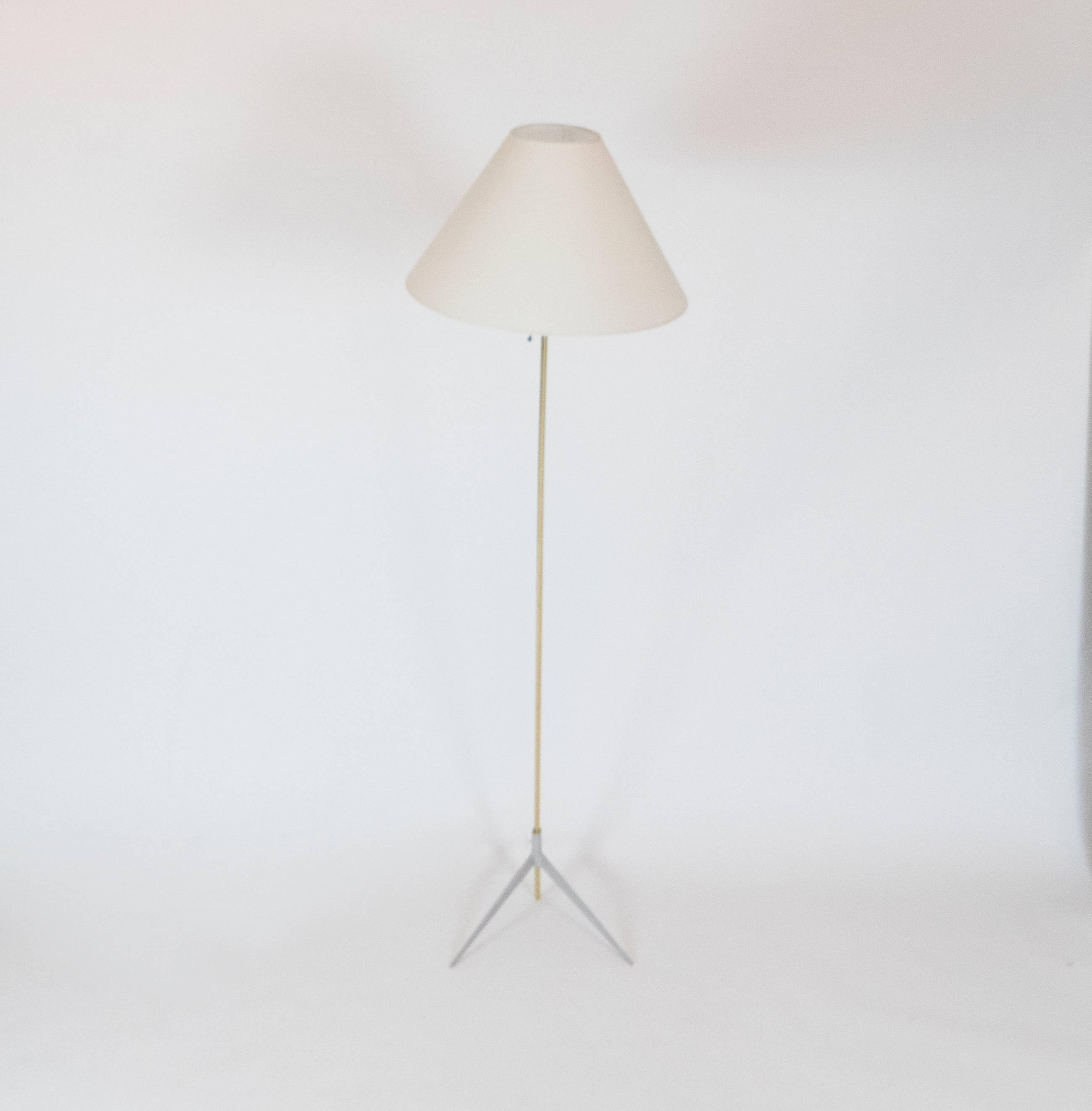 This tripod floor lamp by Giuseppe Ostuni. The gentle tilt of the brass frame and the conic shaped linen shade are sitting on a pair of scissor feet with a grey enamel finish. The light uses on medium based bulb and has an elegant pull switch.