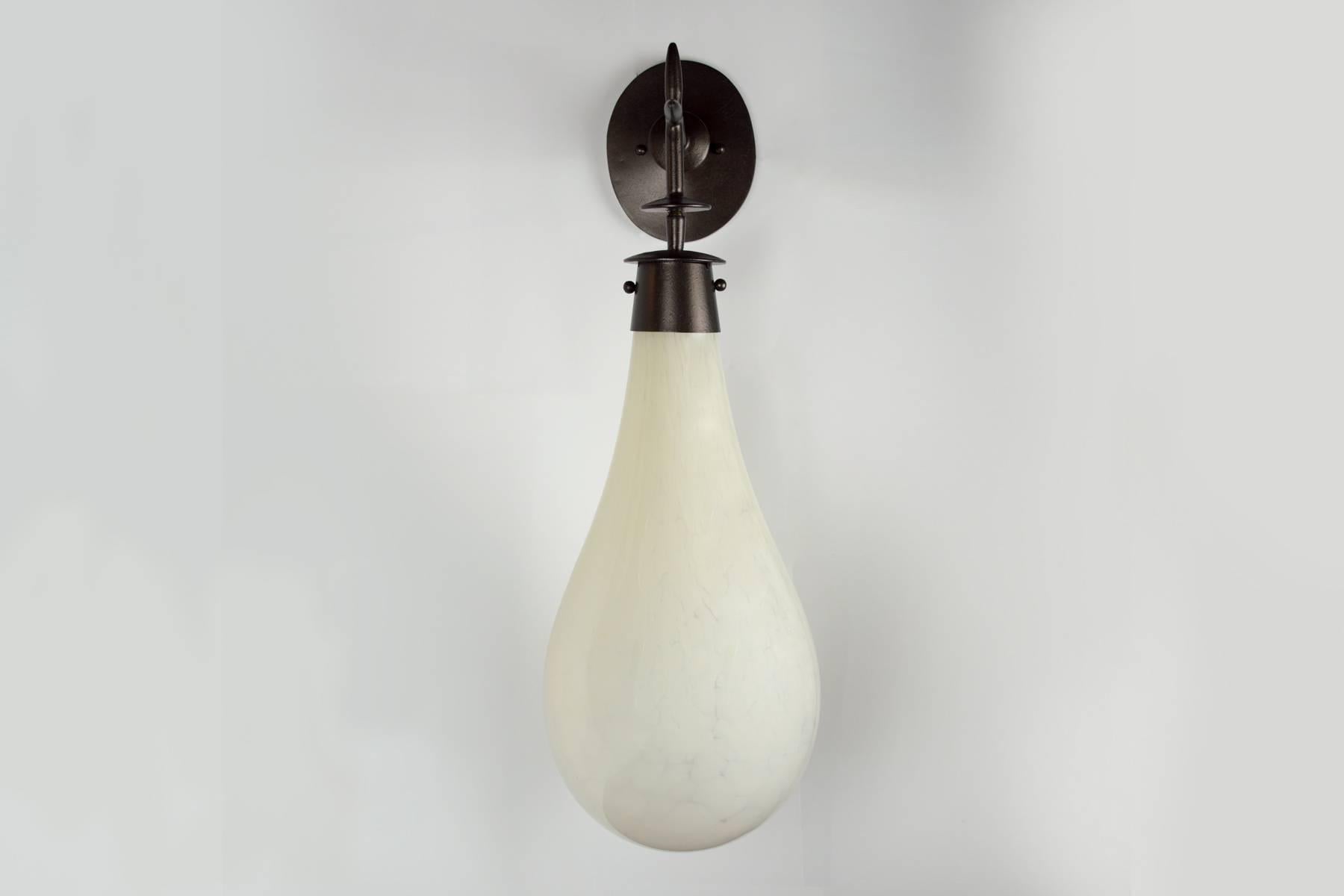 These large-scale sconce have large handblown glass drops which are mounted on a bronze wall mount. Lights are sold with either a white fret or amber colored glass. Each drop is handblown and unique. Lights mount to a standard J box and have one