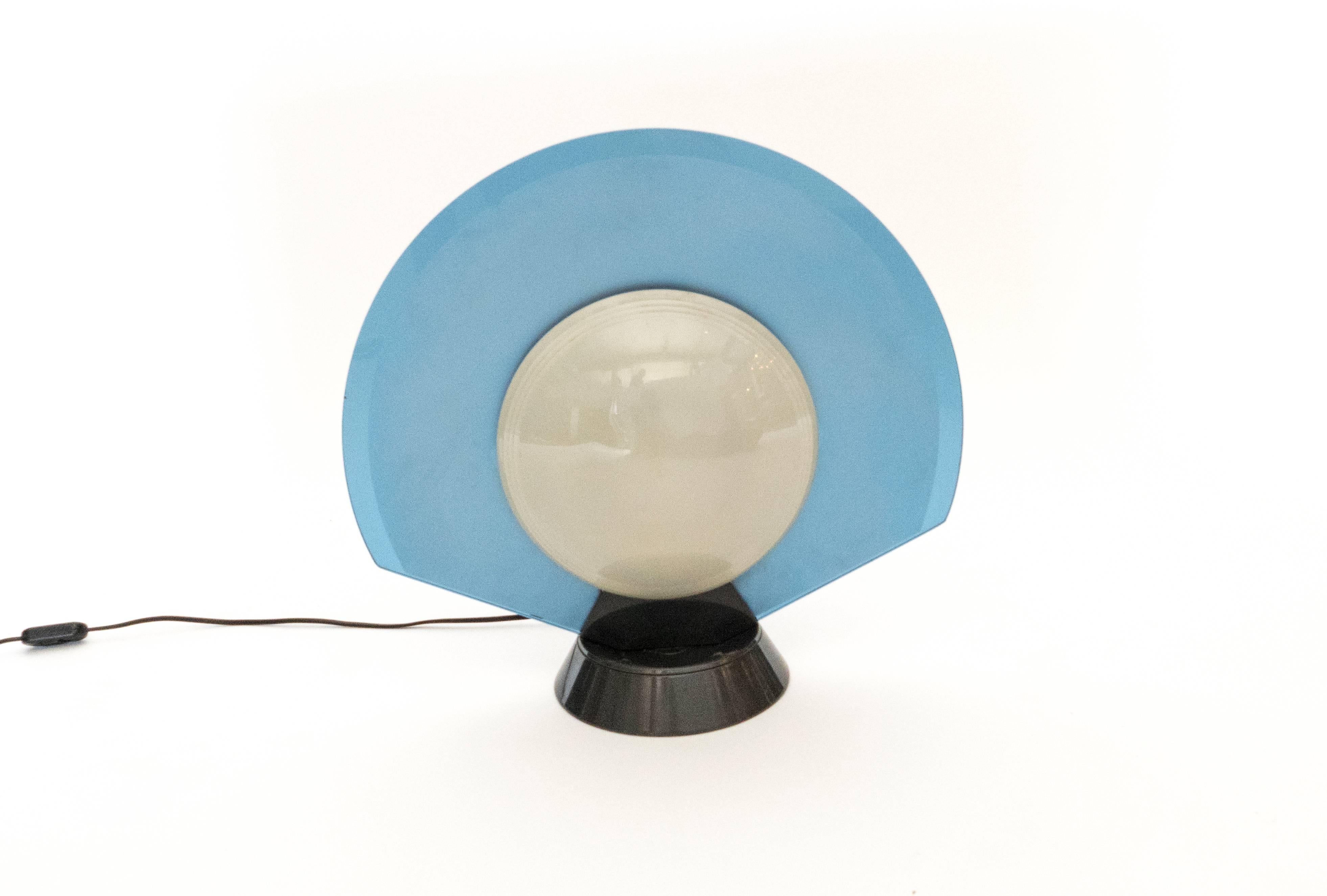 This unique table lamp by Arteluce provides a soft Directional light. The two-sided lamp has one opaque lens and one translucent one. The bronze colored base allows the frosted blue fan to twist and direct the light in all directions. The plastic