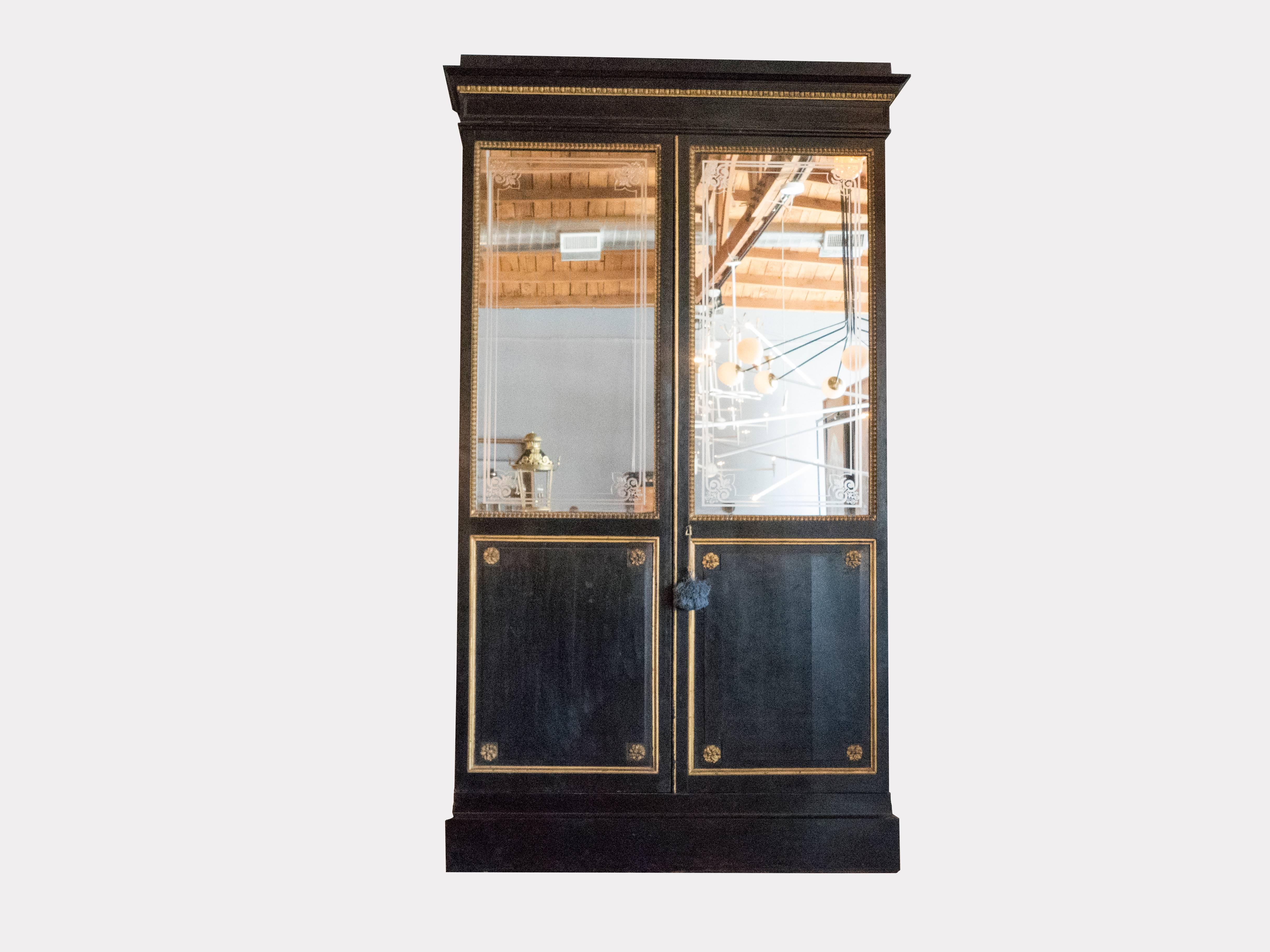 This impressive cabinet has it original etched mirrored doors and gilded carved wood accents. It is in great condition and will create a real statement. The cabinet has an ebony finish of the exterior oak frame. Six adjustable shelves.  This item is