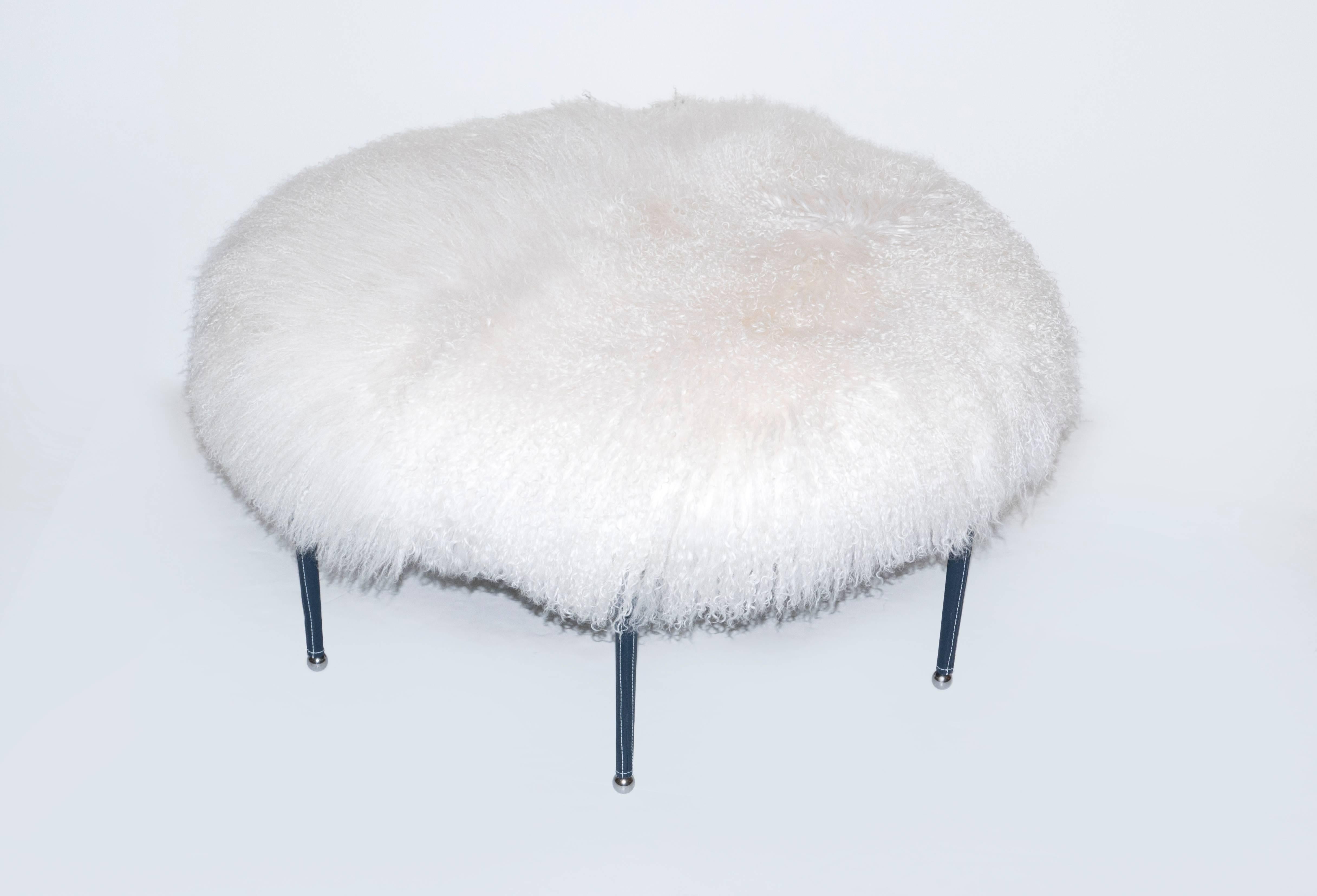 Large round ottoman with white Mongolian wool upholstery. The six legs are wrapped in stitched navy blue leather with steel accents.  Bench is located our NYC showroom.