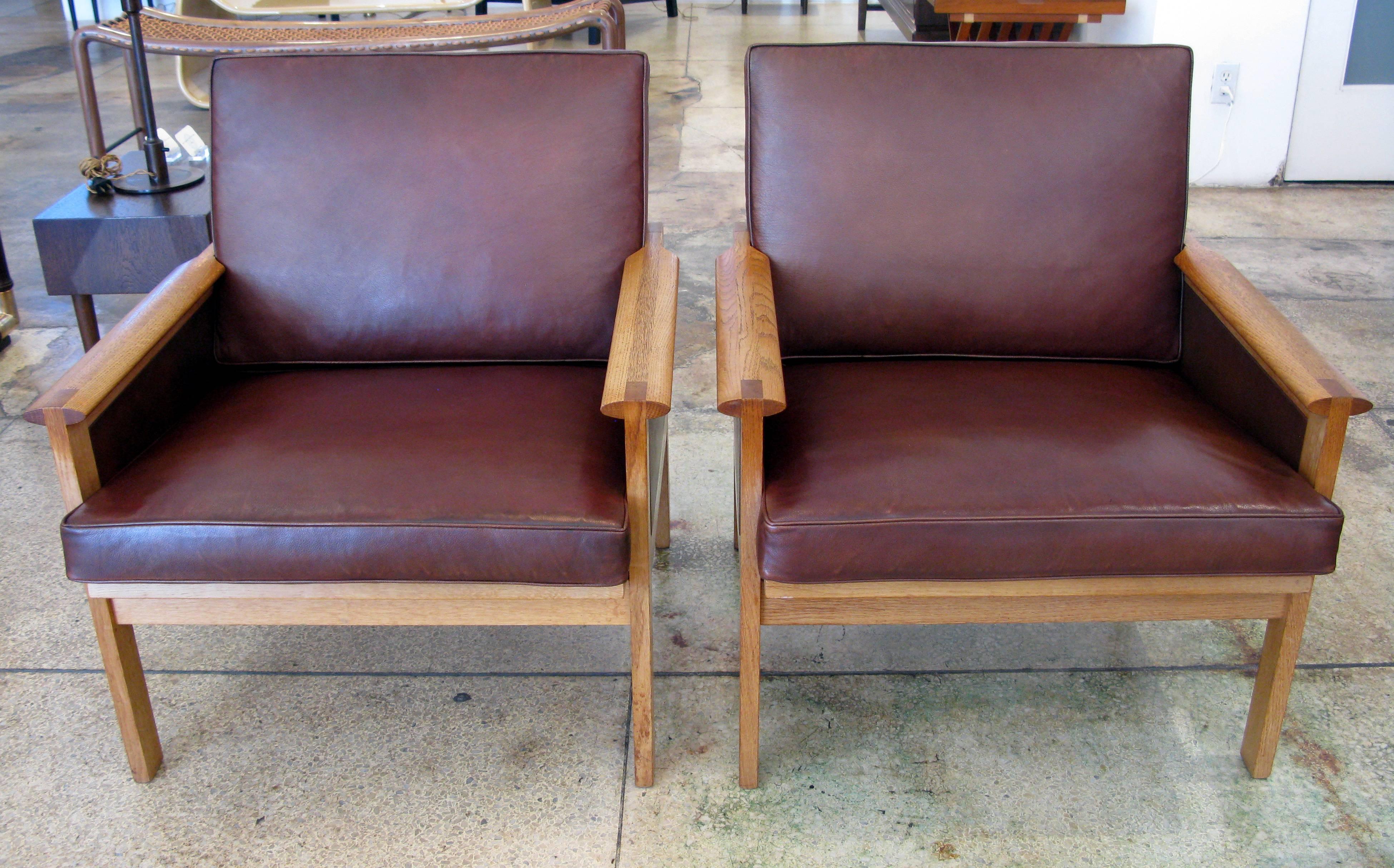 Pair of rare leather and oak lounge chairs designed by Illum Wikkelsø for N. Eilersen, Denmark. Chocolate brown leather cushions and side panels with a subtle reddish undertone. Seat height: 16