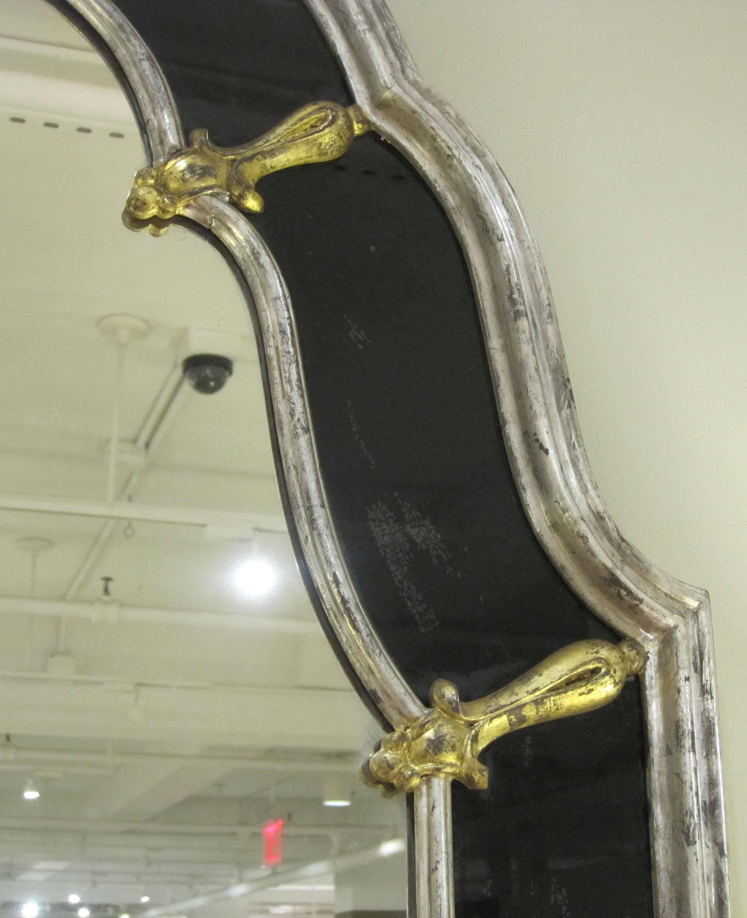 A glamorous American Hollywood Regency, 1960s silver giltwood mirror with black glass border; the arching silver giltwood double from with gold leaf spandrels; surrounding a conforming mirror plate with black glass border.