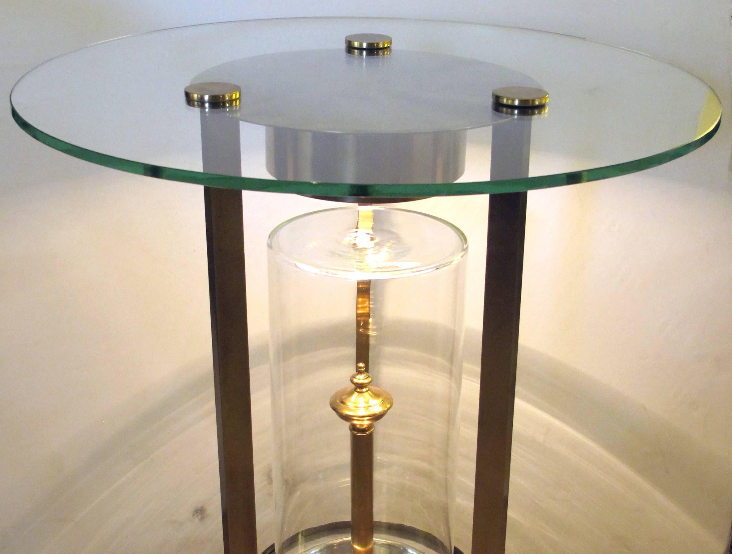 A rare pair of American, 1950s glass and brass illuminated circular side tables, designed by Dorothy Thorpe for the USS Enterprise Steamship lounge, each circular glass top secured with three solid brass discs, raised on three slender supports