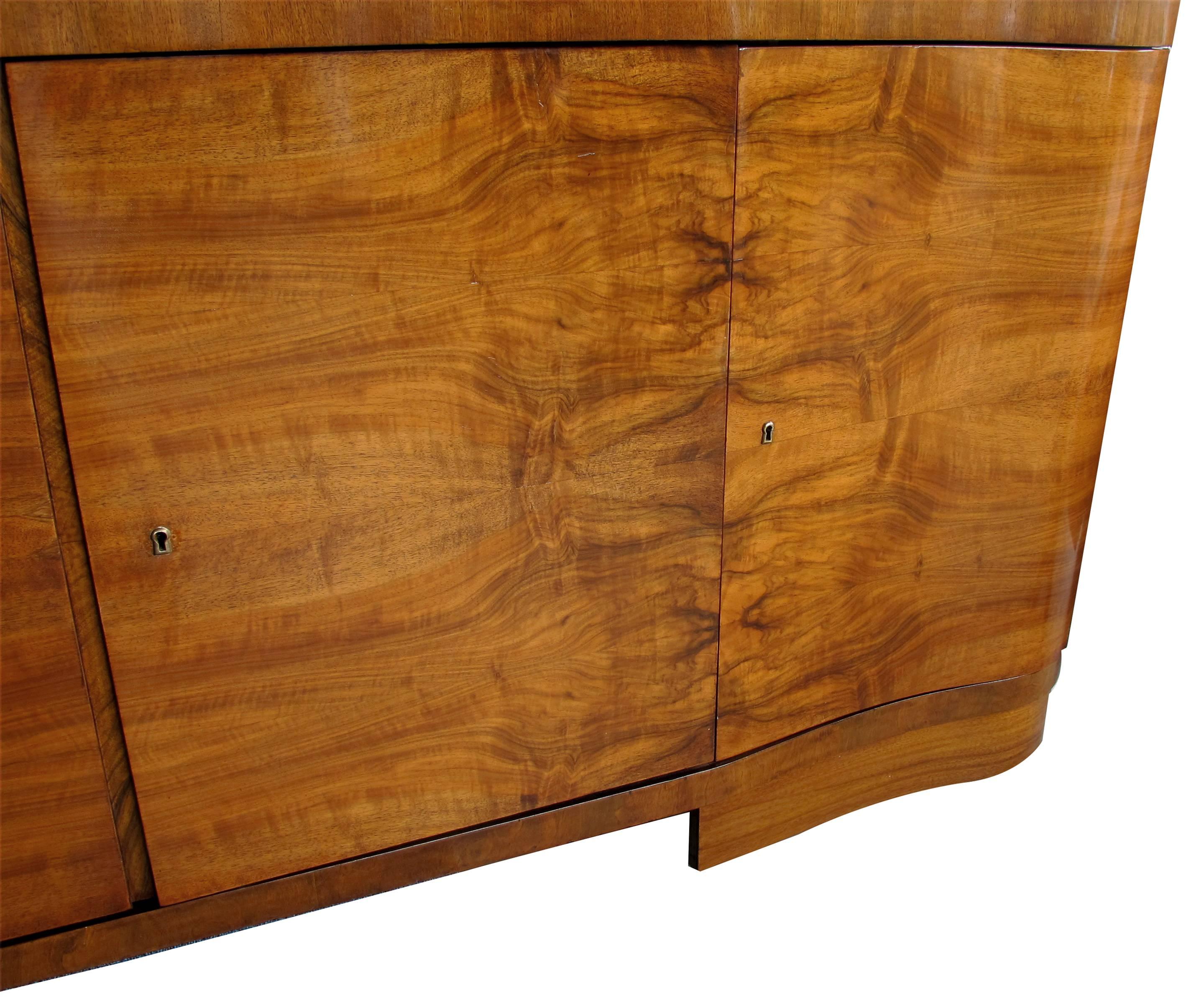 A large-scaled and well veneered English Art Deco walnut four-door sideboard, the scalloped top over a conforming body all in a well-figured matchbook walnut veneer.
