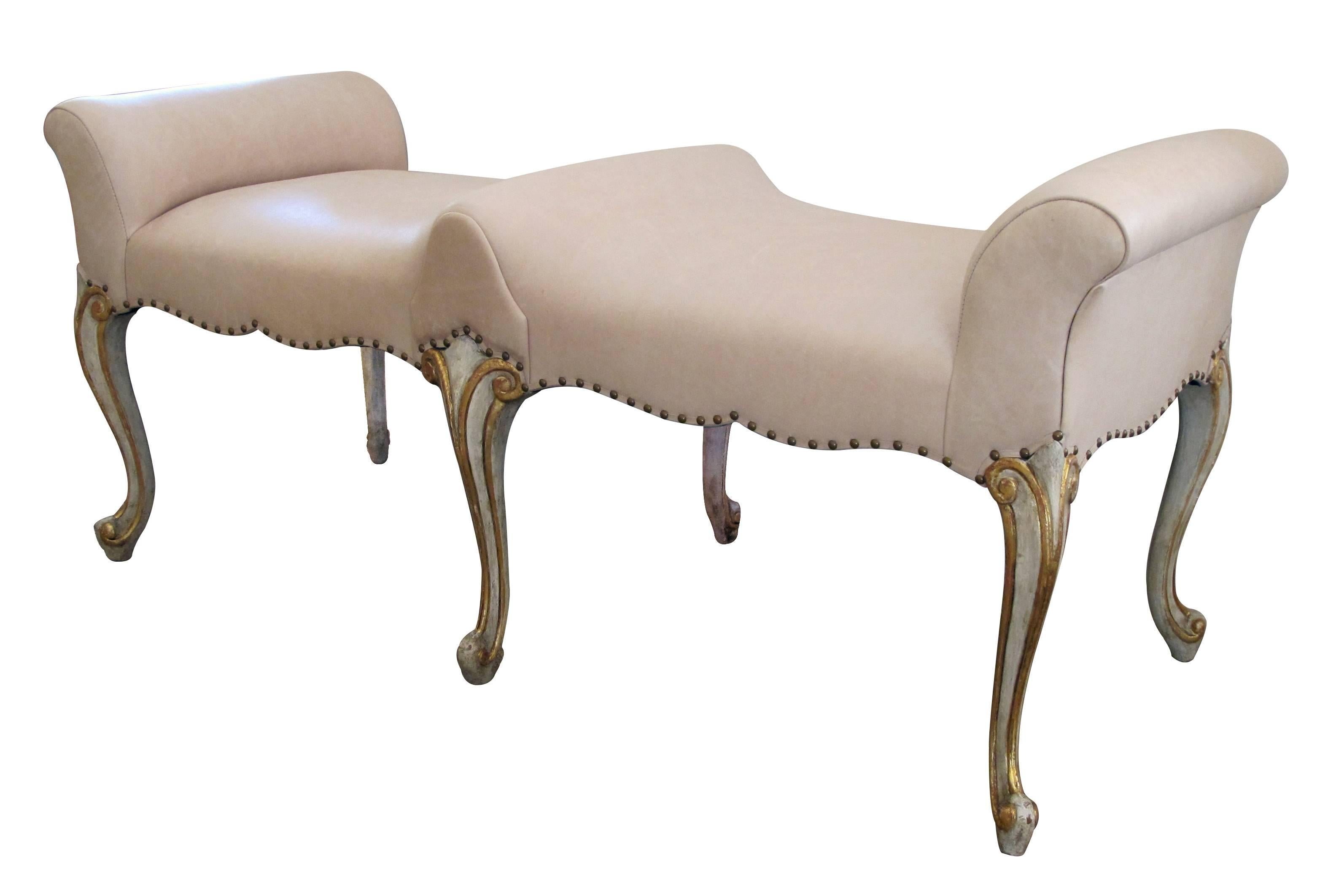 A shapely French Louis XV style pale green painted and parcel-gilt double-seated bench; the long double-seated bench with scrolled arms above a scalloped apron; raised on elegant cabriole supports; new tan leather upholstery.