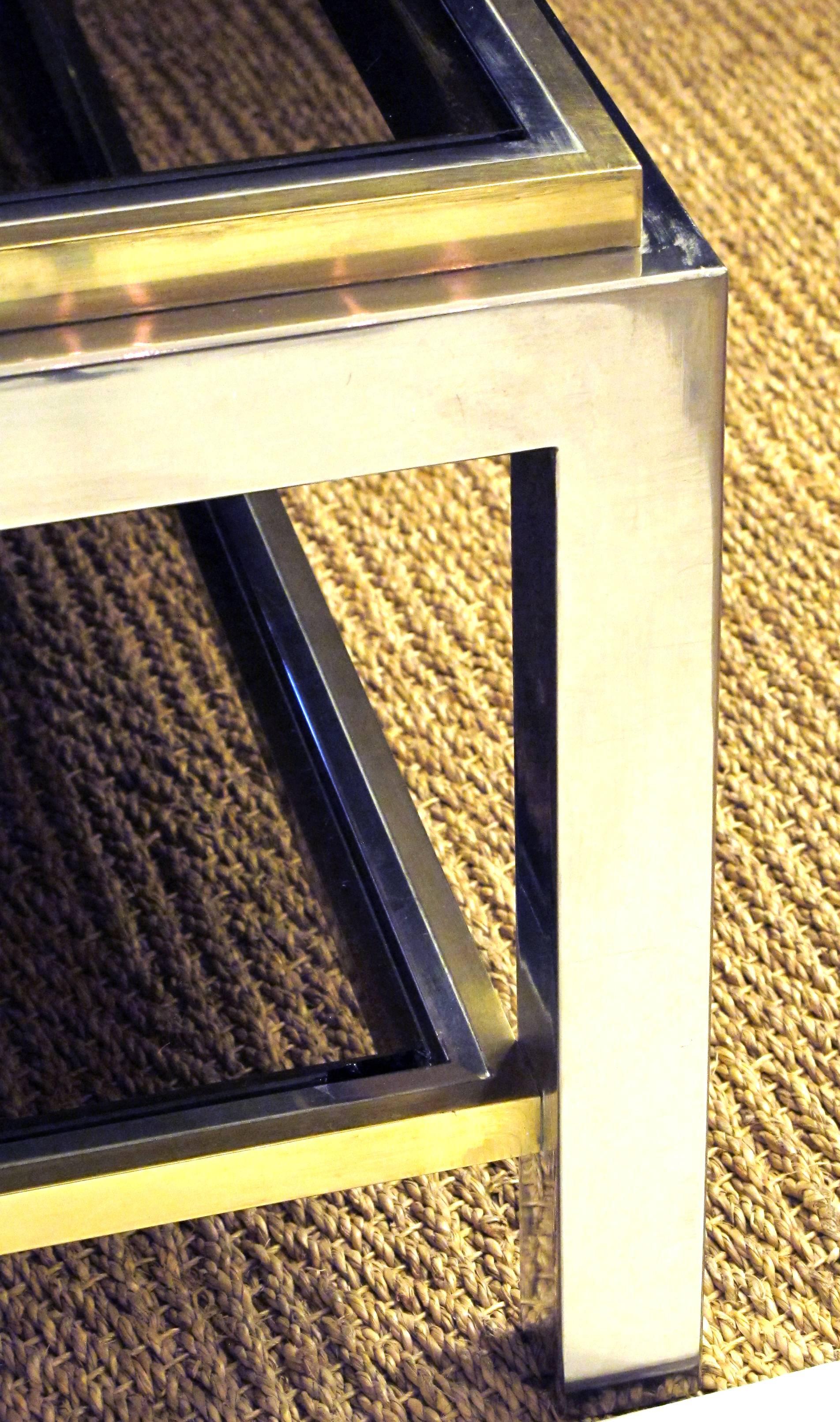 Table basse carrée en laiton patiné et nickel poli, signée Jean Charles, datant des années 1970, avec plateau en verre fumé et étagère inférieure ; le grand plateau carré en verre inséré dans un cadre en chrome et laiton repose sur des supports
