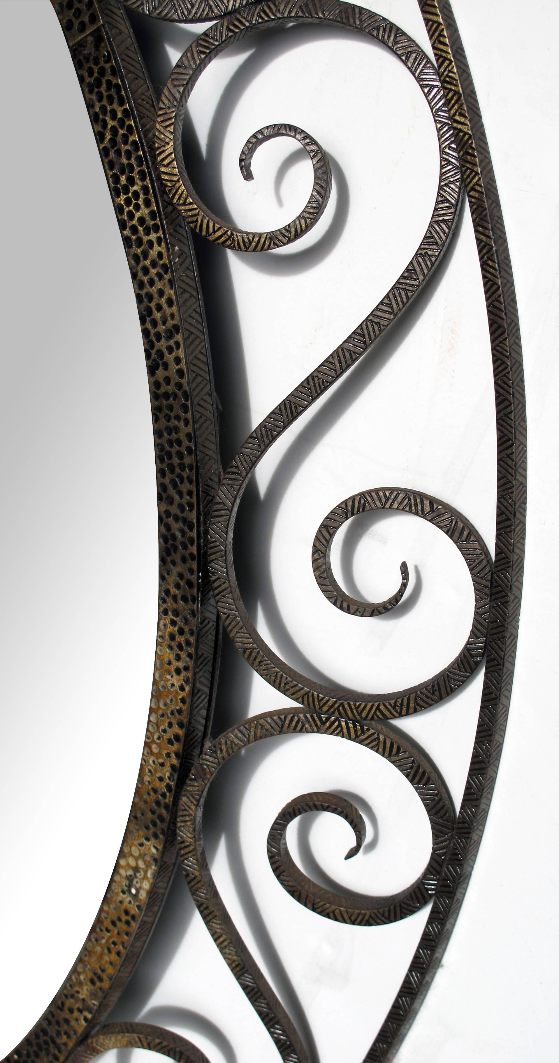 A hand-crafted French art deco openwork iron oval mirror in the style of Edgar Brandt; the oval plate within a punched iron border surrounded by a sloping openwork frame of graceful s-curves
