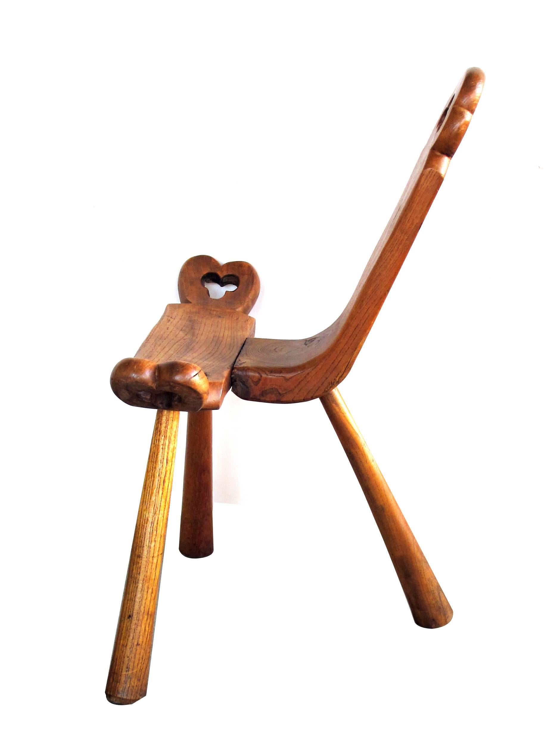 A delightful and rustic pair of Swiss Tyrolean waxed oak mountain stools; each with pierced back and seat with trefoil motif raised on three turned, graduated supports.