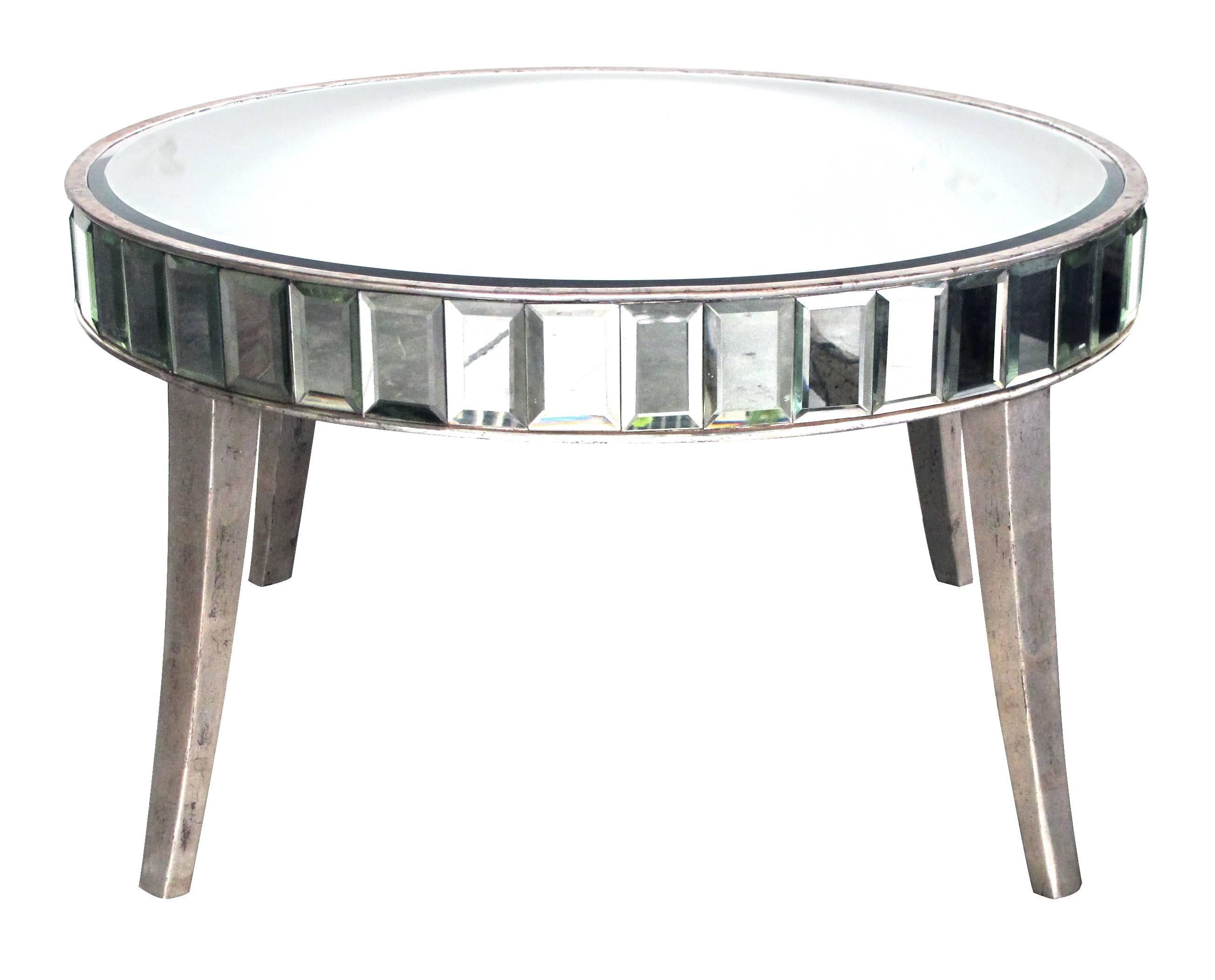 A shimmering American Mid-Century circular mirrored coffee/cocktail table with silver giltwood supports; the round beveled mirrored top above an apron composed of beveled mirrored panels; raised on gracefully splayed giltwood legs.
