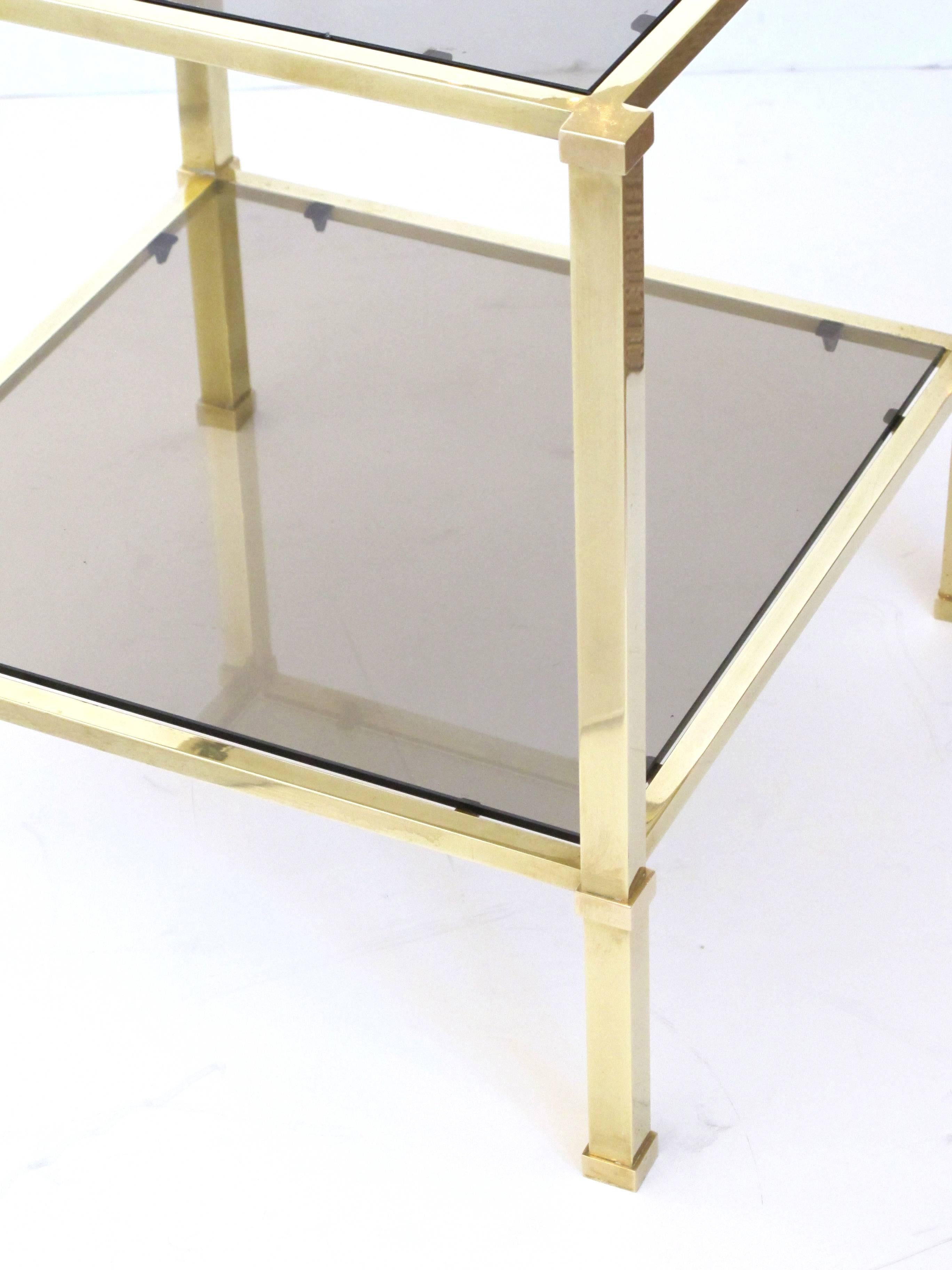 A good quality pair of French 1970s solid brass and smoked glass square side tables; each inset glass top within a solid brass frame raised on quadrangular supports joined by a lower glass shelf.