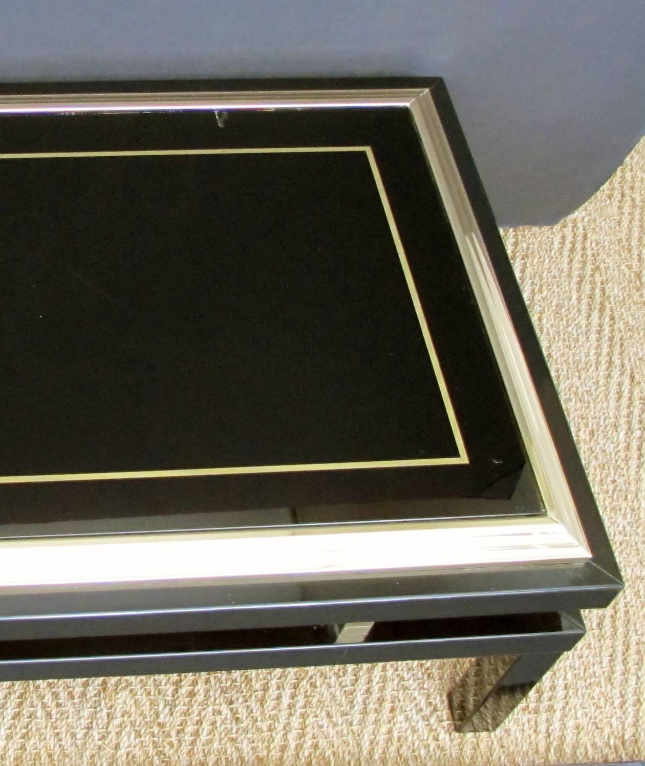 A stylish French 1970s black enameled metal rectangular coffee or cocktail table with brass detailing and églomisé glass top by Guy Lefevre for Maison Jansen; the black glass top with gold églomisé painted striping; within a stepped brass frame