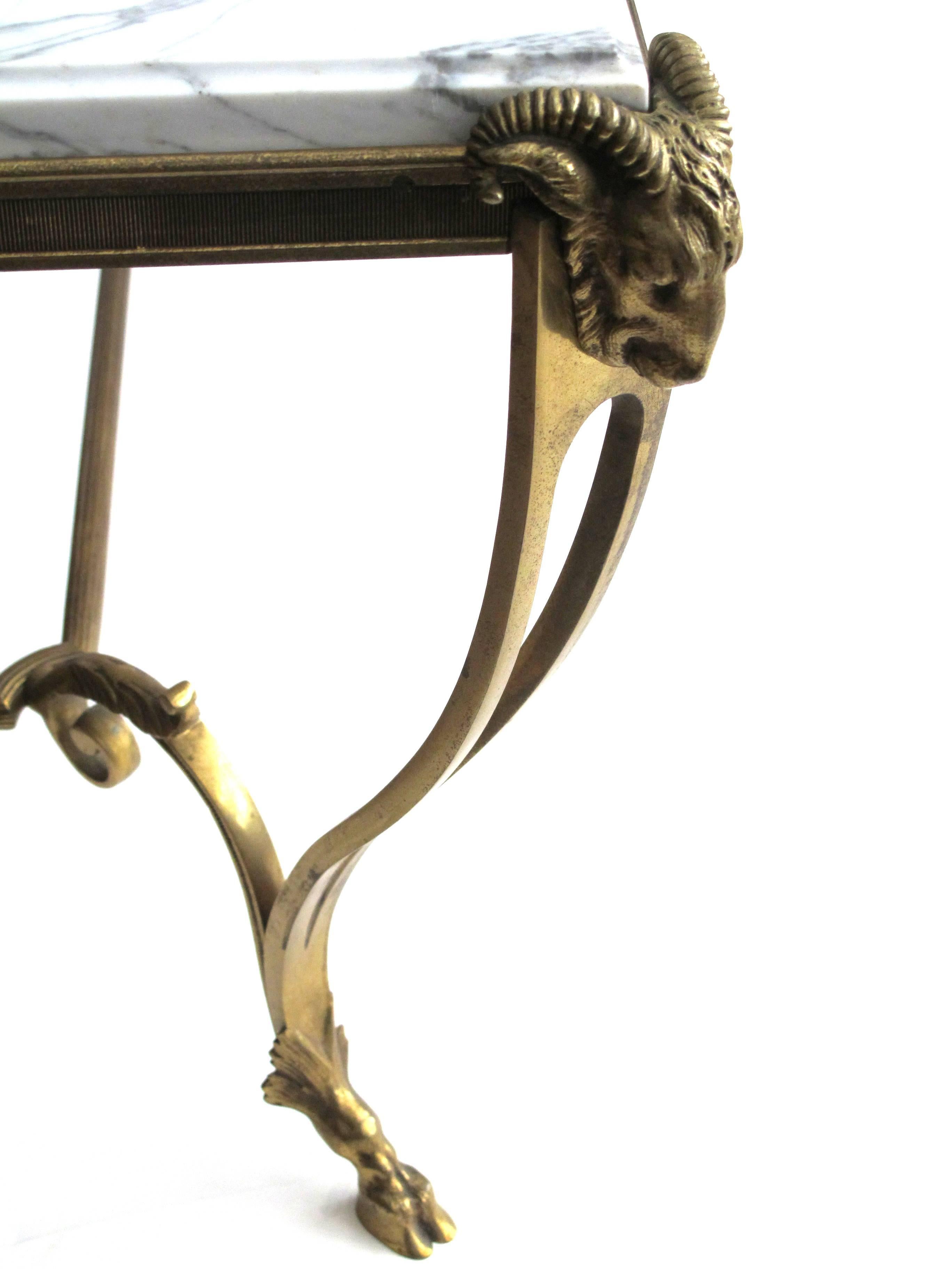 An elegant and good quality French, Maison Bagues, 1940s, gilt bronze coffee/cocktail table with hoofed feet and Carrera marble top, the well-veined top within a gilt bronze frame raised on elegantly scrolled supports with ram's head caps ending in