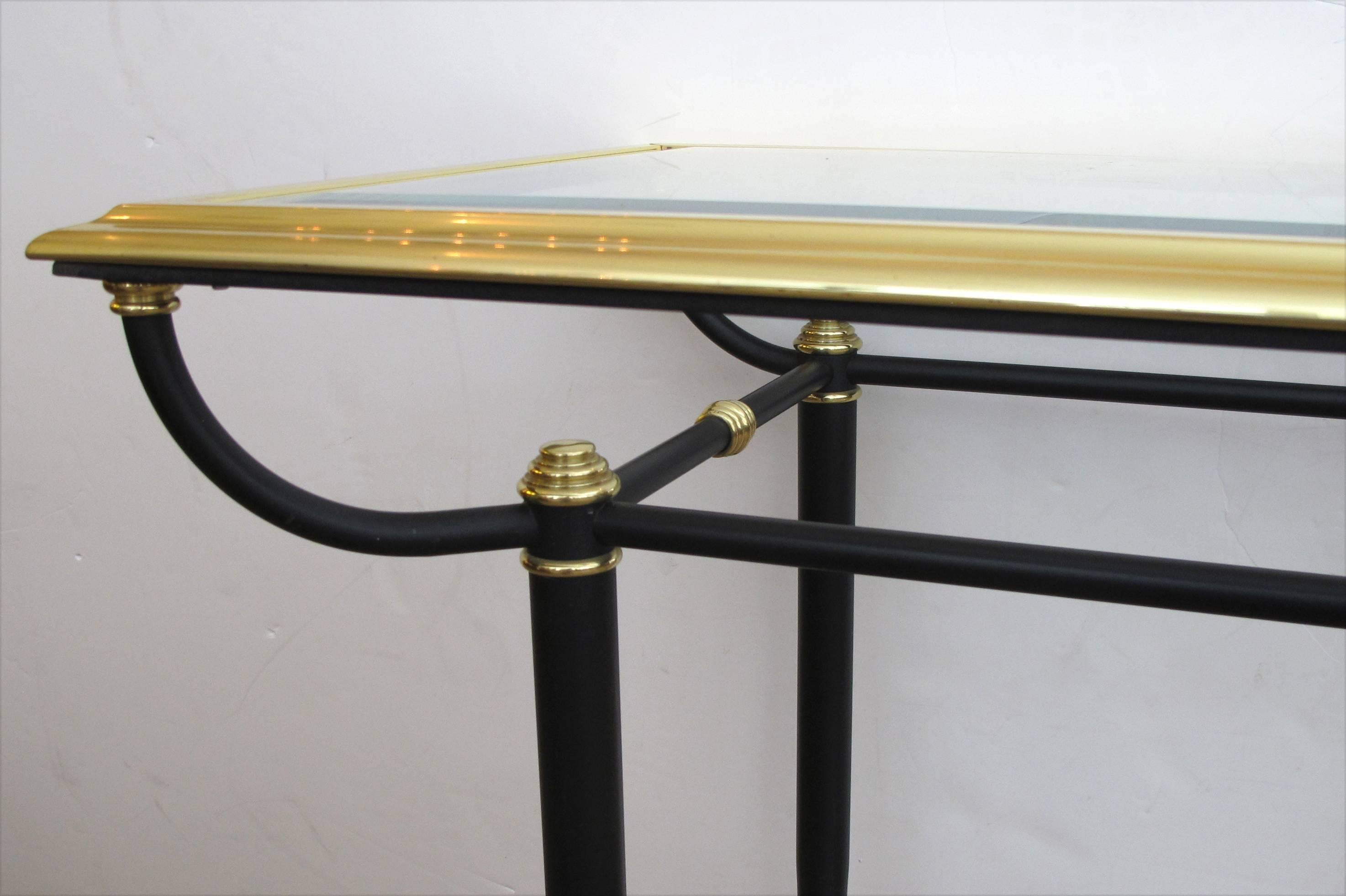 A good quality French 1960s brass and black console table with beveled glass top and lower shelf; the long inset glass top within a molded brass border; raised on a black metal base joined by a lower glass shelf.